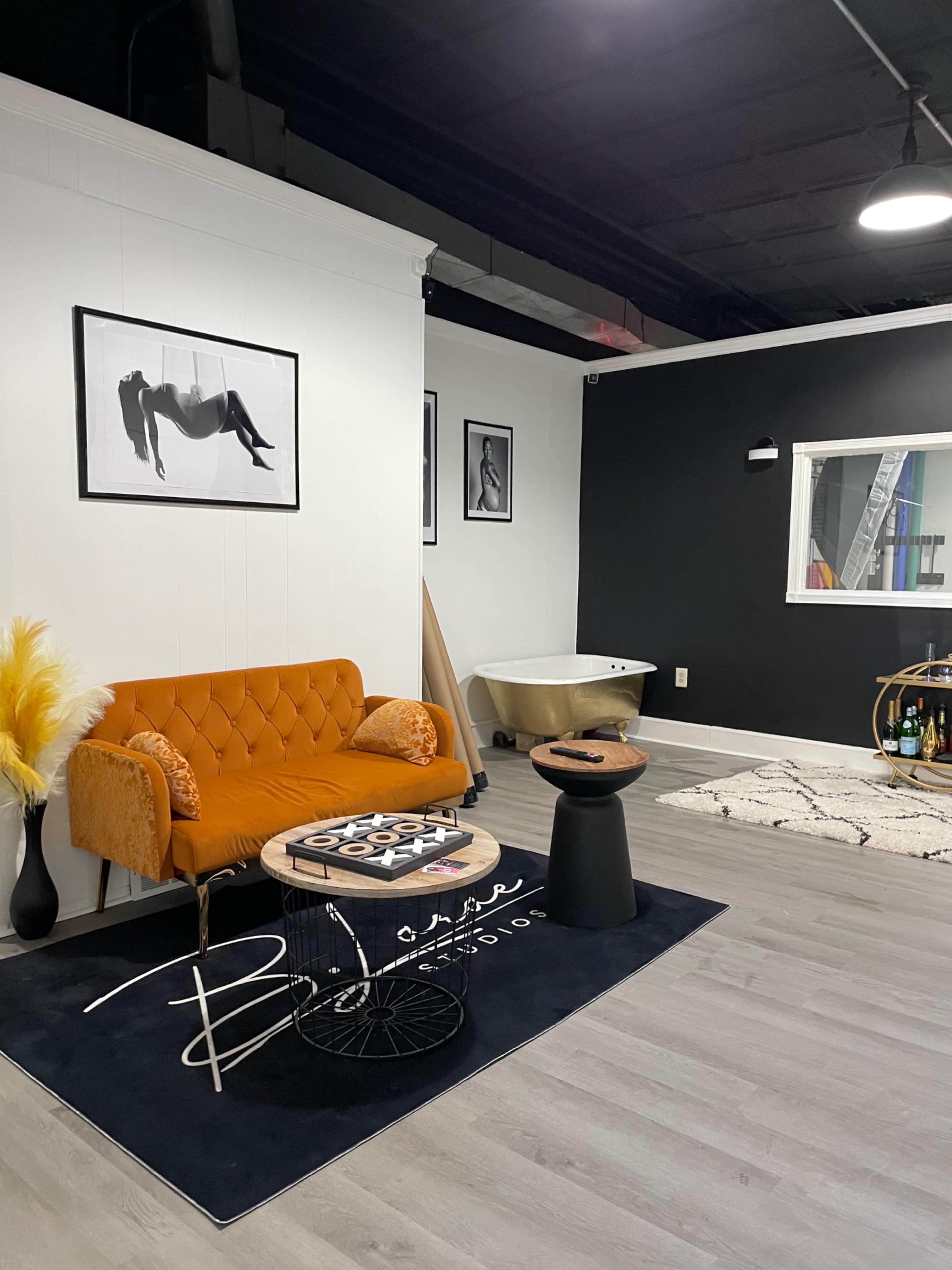 The image shows a modern interior space featuring an orange couch, a round table, a black wall, and a clawfoot bathtub in the background.