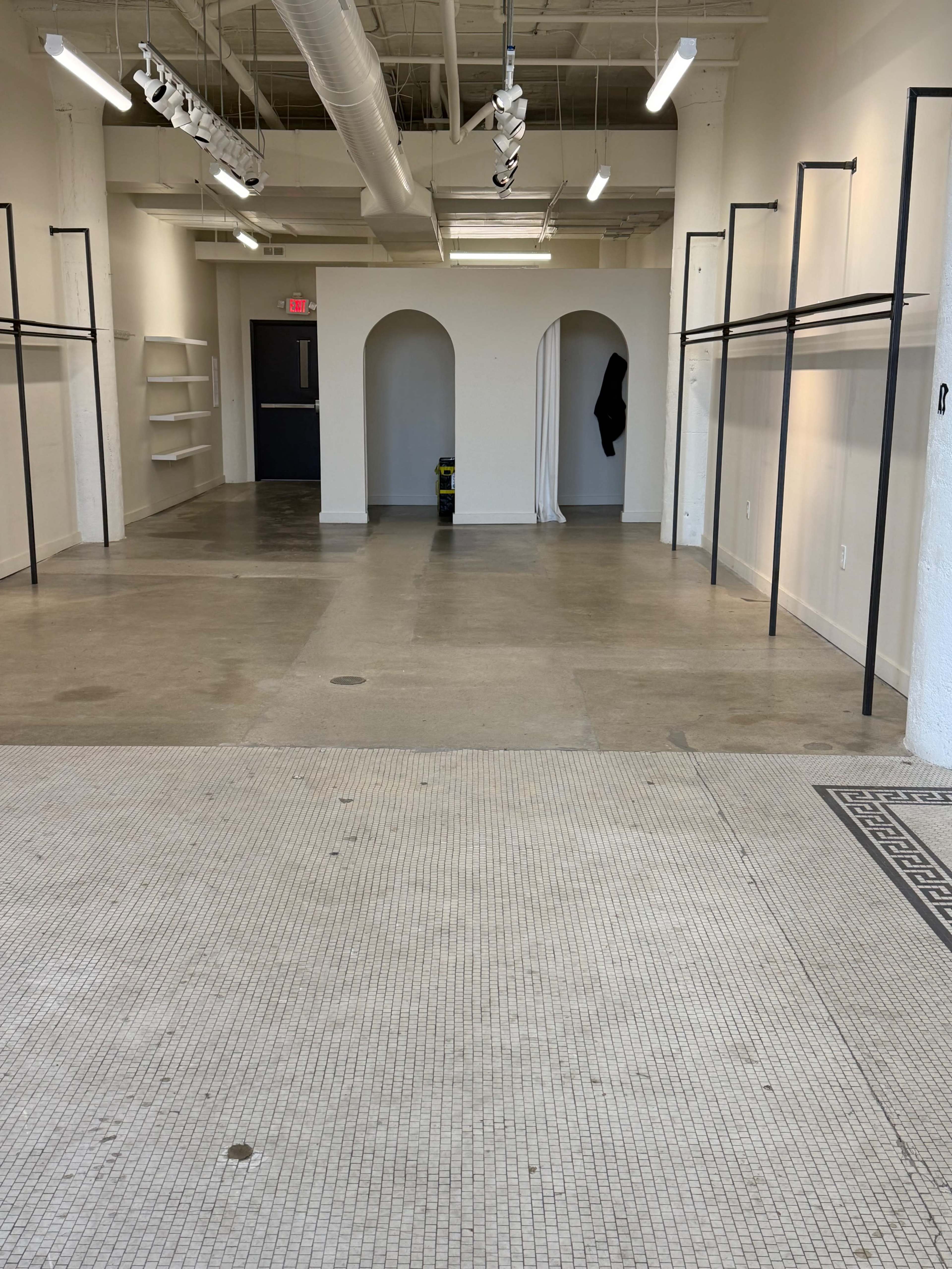 The image shows an empty interior space with a tiled floor, white walls, and two archways visible in the background.