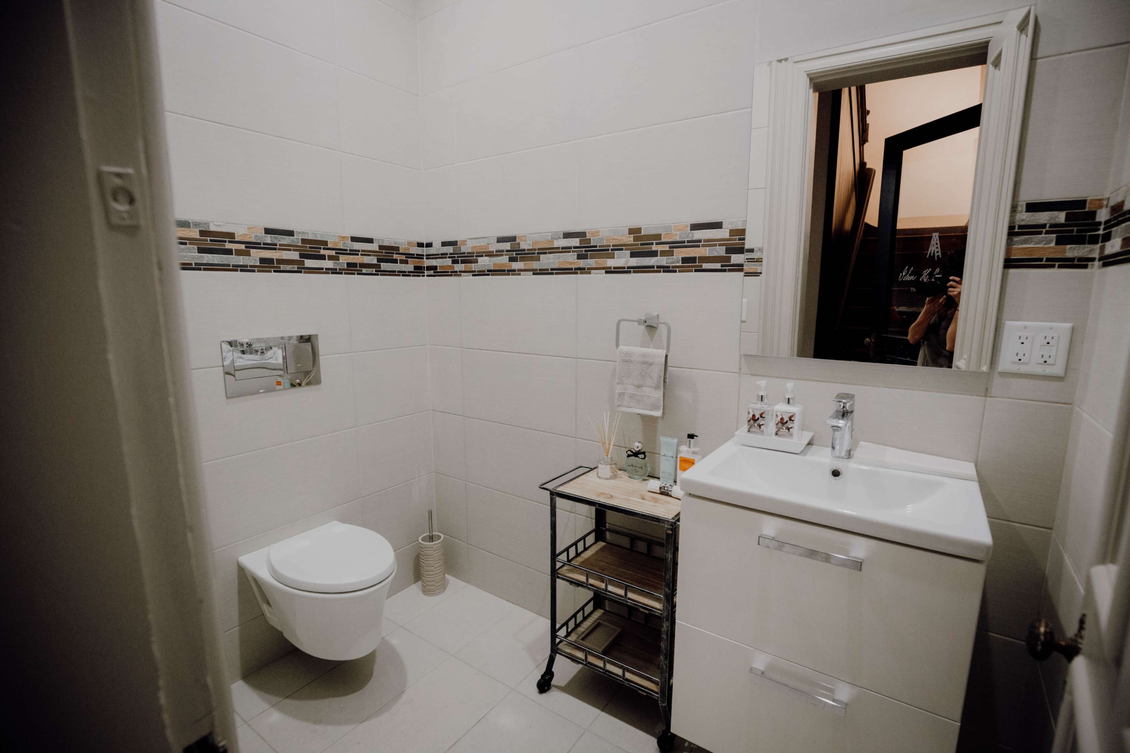 A modern bathroom featuring a wall-mounted toilet, a sink with storage underneath, and decorative tiles along the middle of the walls.