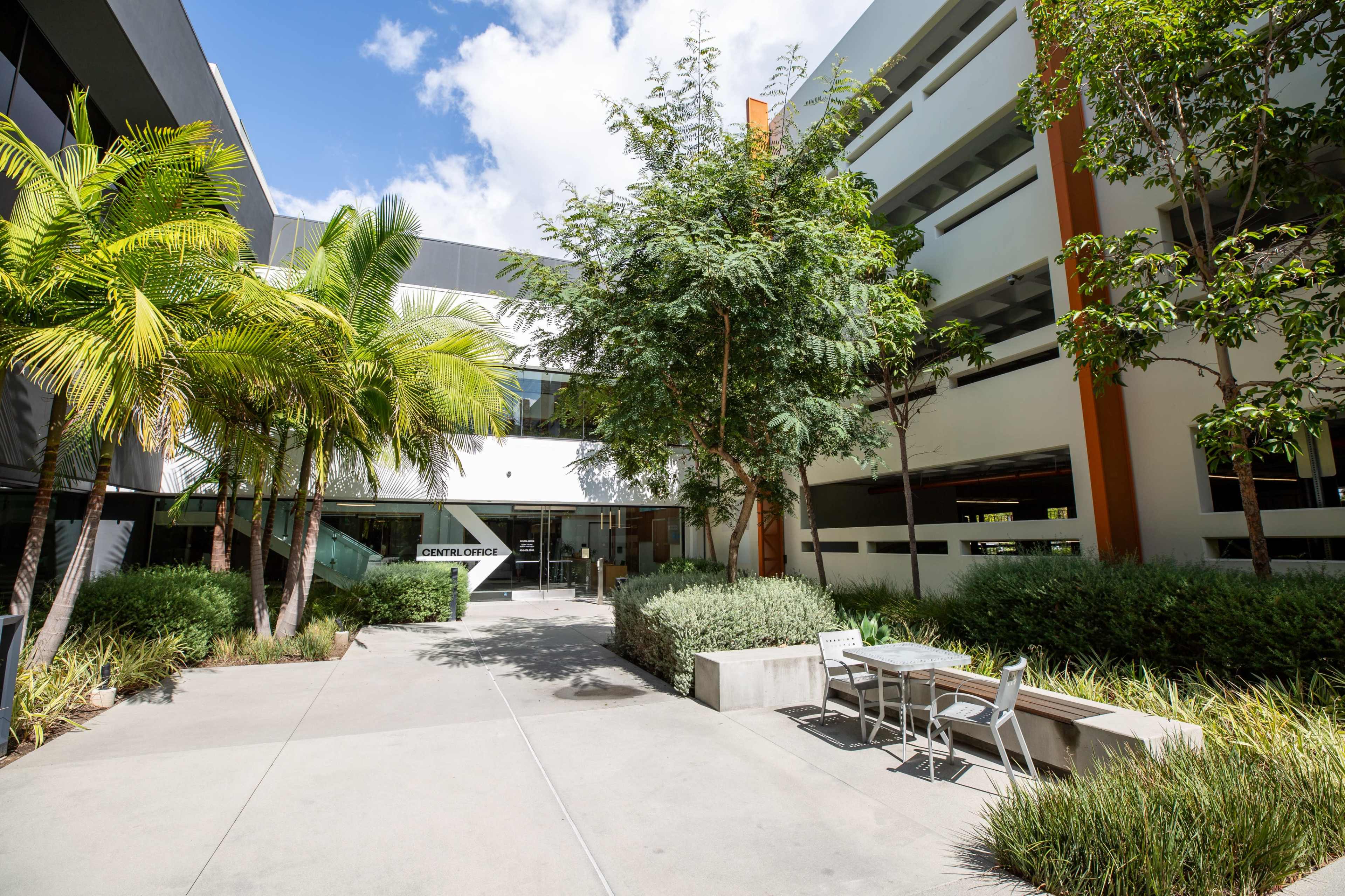 A modern building entrance surrounded by greenery and outdoor seating.