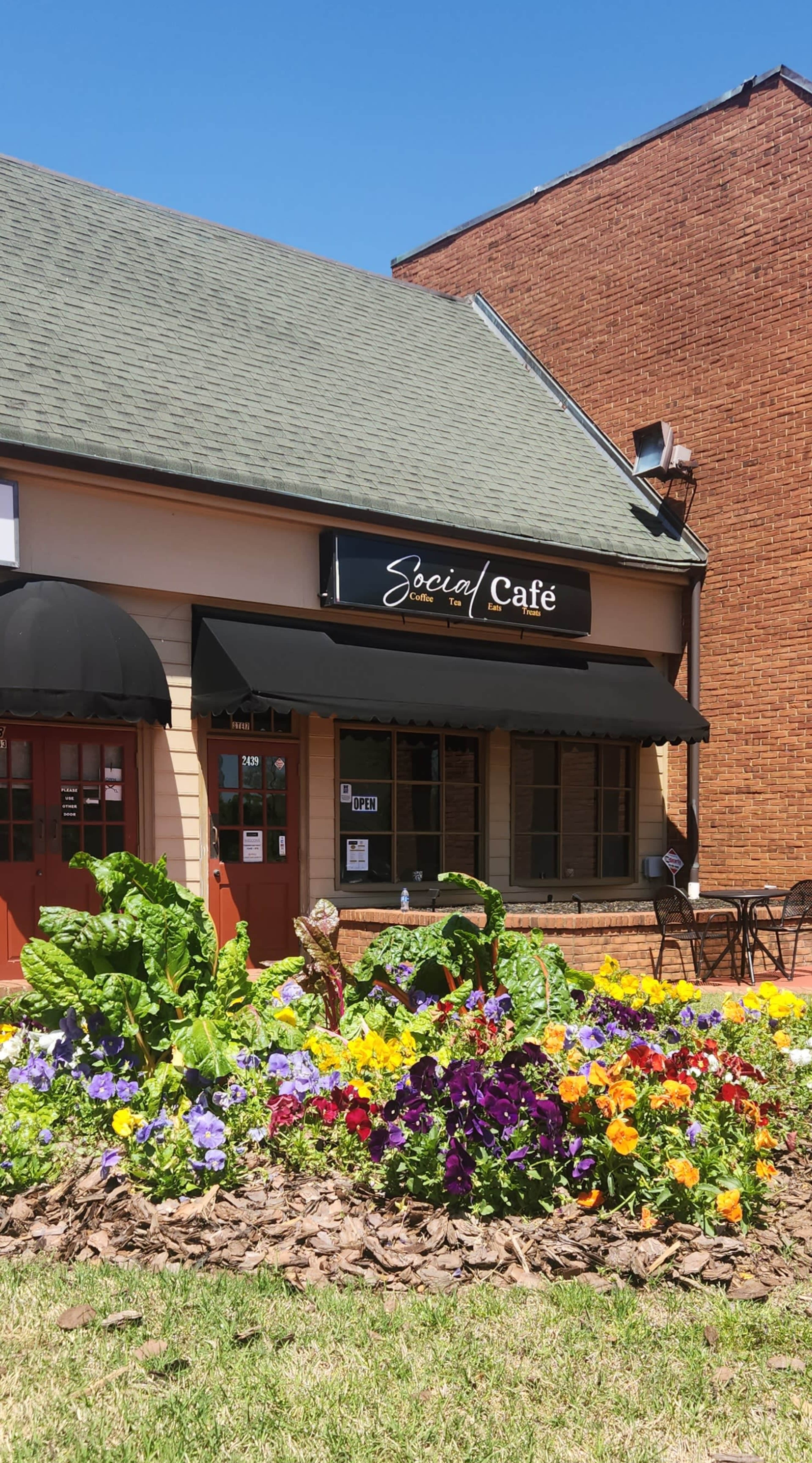 The image shows the storefront of Social Café, featuring a welcoming entrance and a colorful flower bed in front.