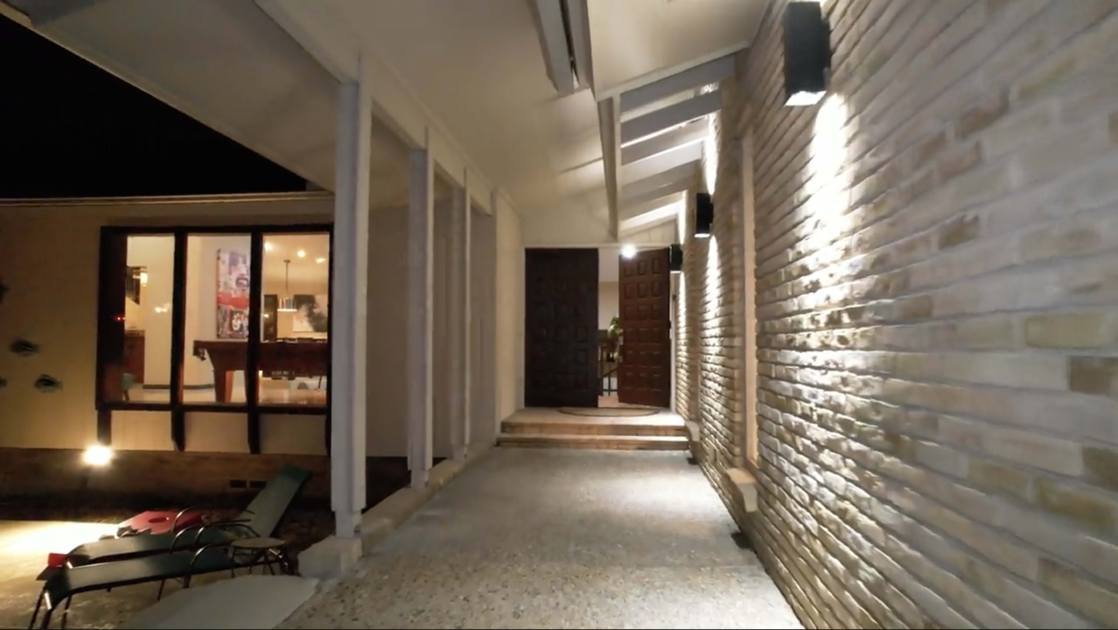 A well-lit entrance leading to a front door, with a pathway alongside a stone wall and a window revealing an indoor space.