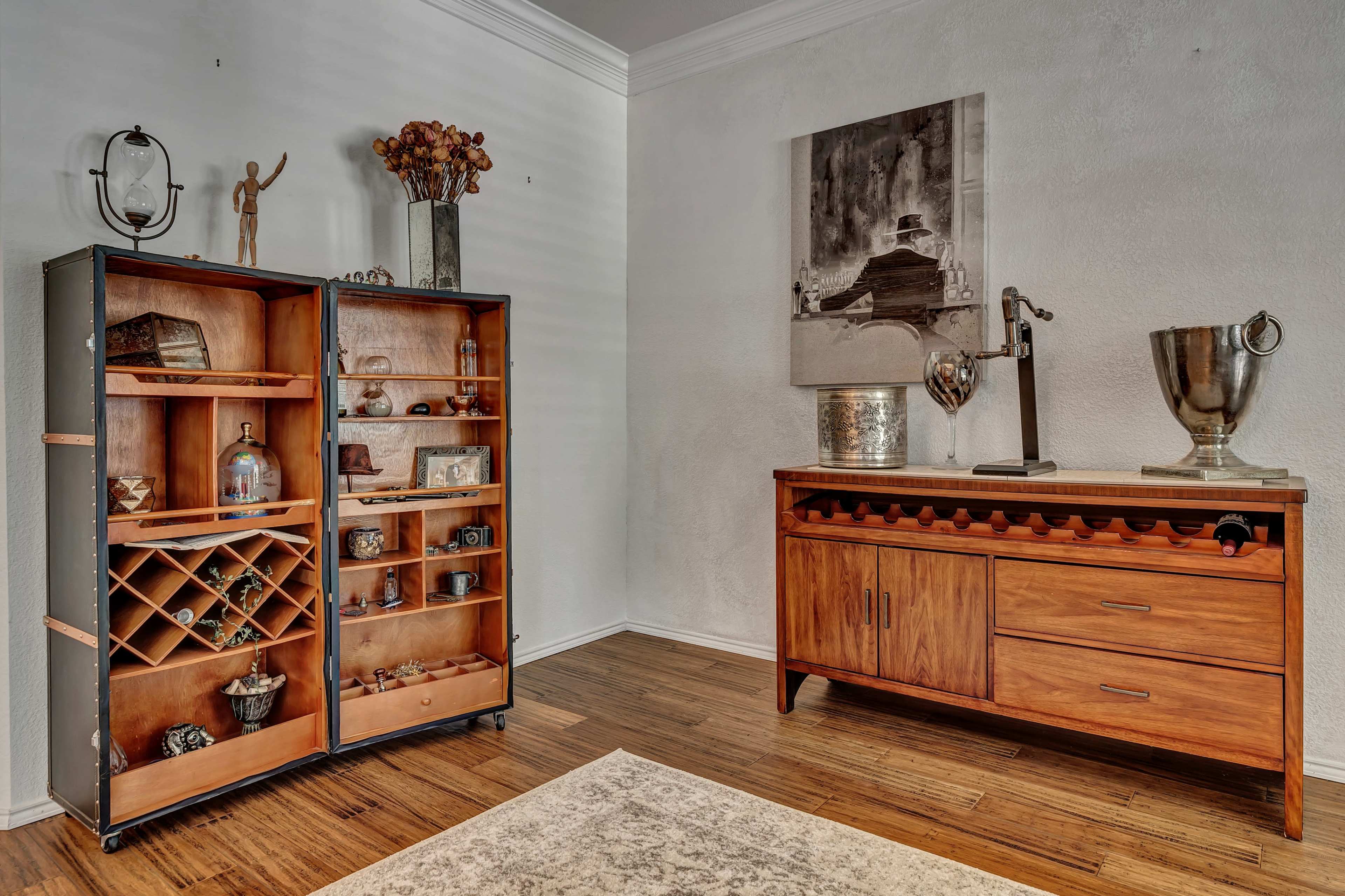 A modern interior space featuring a wooden display cabinet with shelves and a wine rack on the left and a wooden sideboard with drawers and a decorative piece on the right.