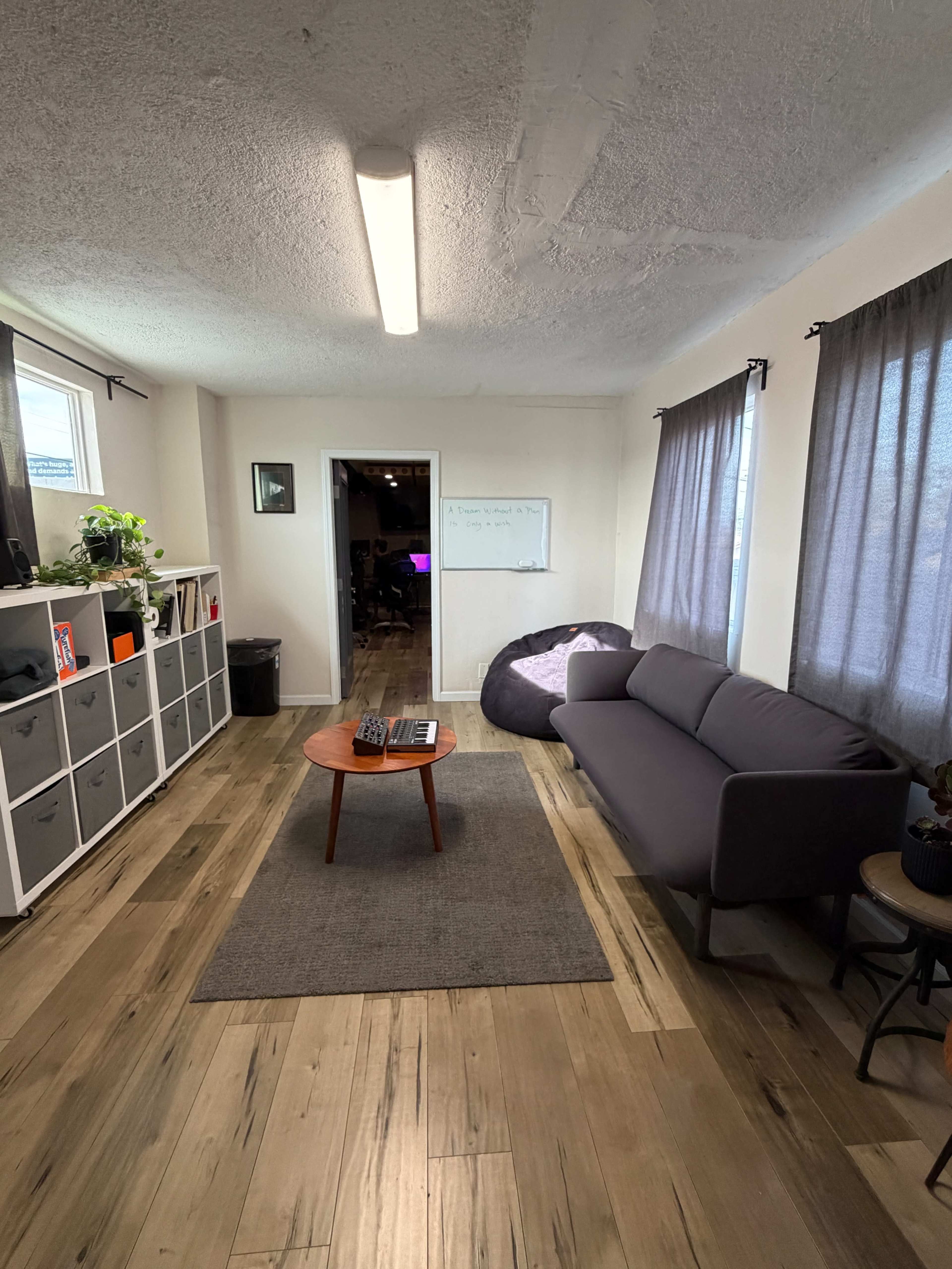 The image shows a minimalist living space featuring a gray sofa, a coffee table with a keyboard, a rug, and shelves with storage boxes along one wall.