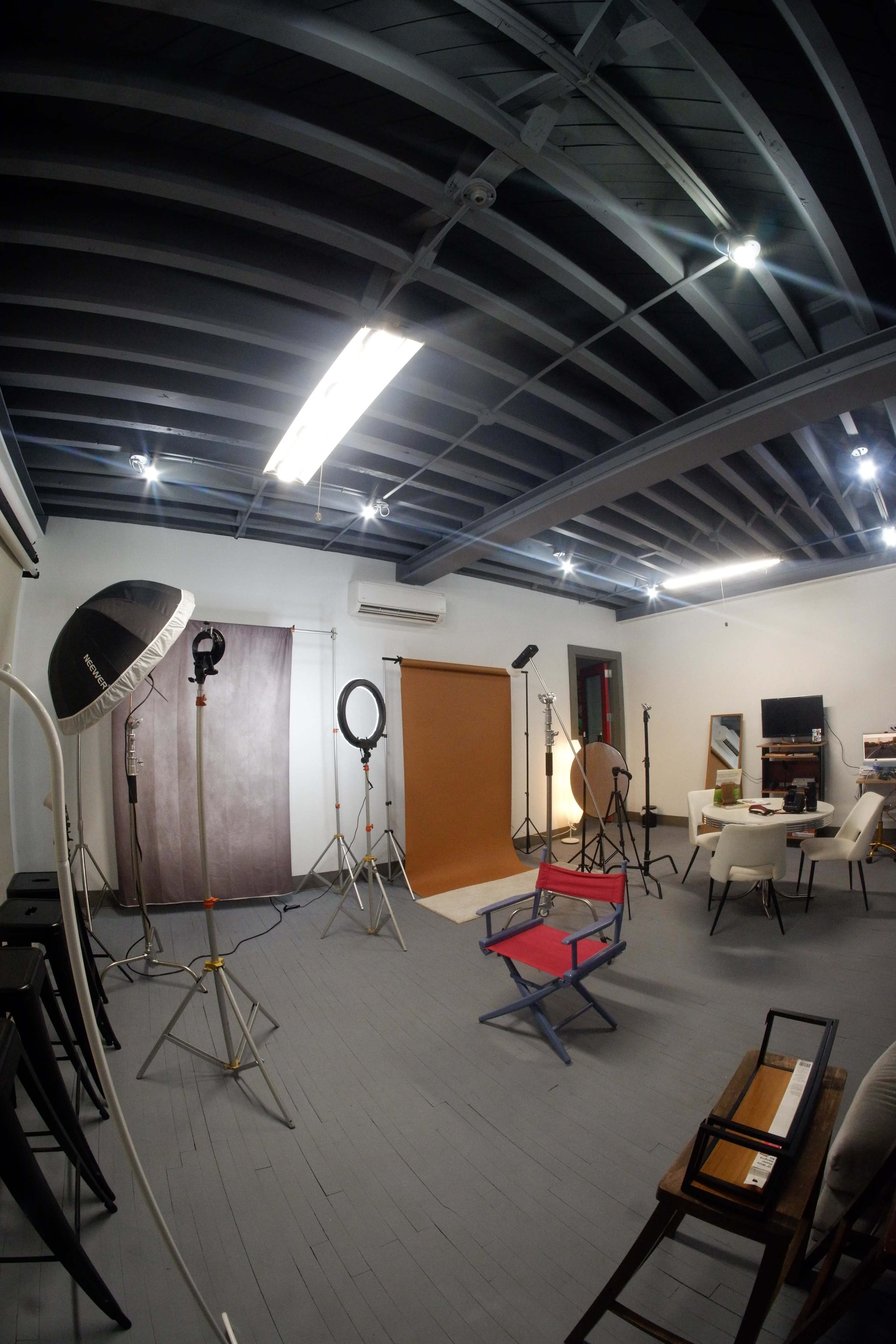The image shows a photography studio with various lighting equipment, backdrops, and seating arranged in a spacious interior.
