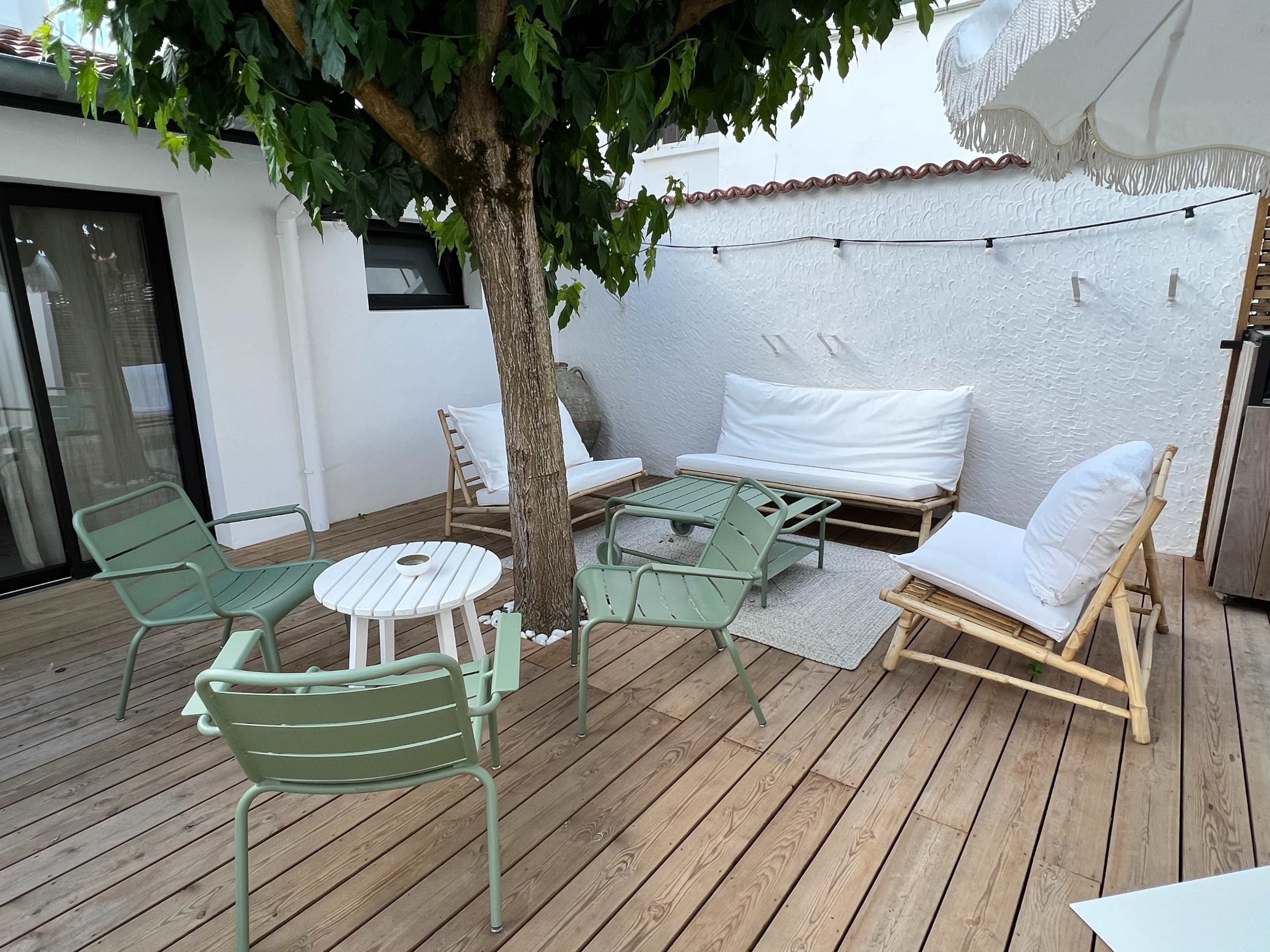 The image shows a wooden deck area with a tree, featuring several seating arrangements, including a sofa, chairs, and a small table.