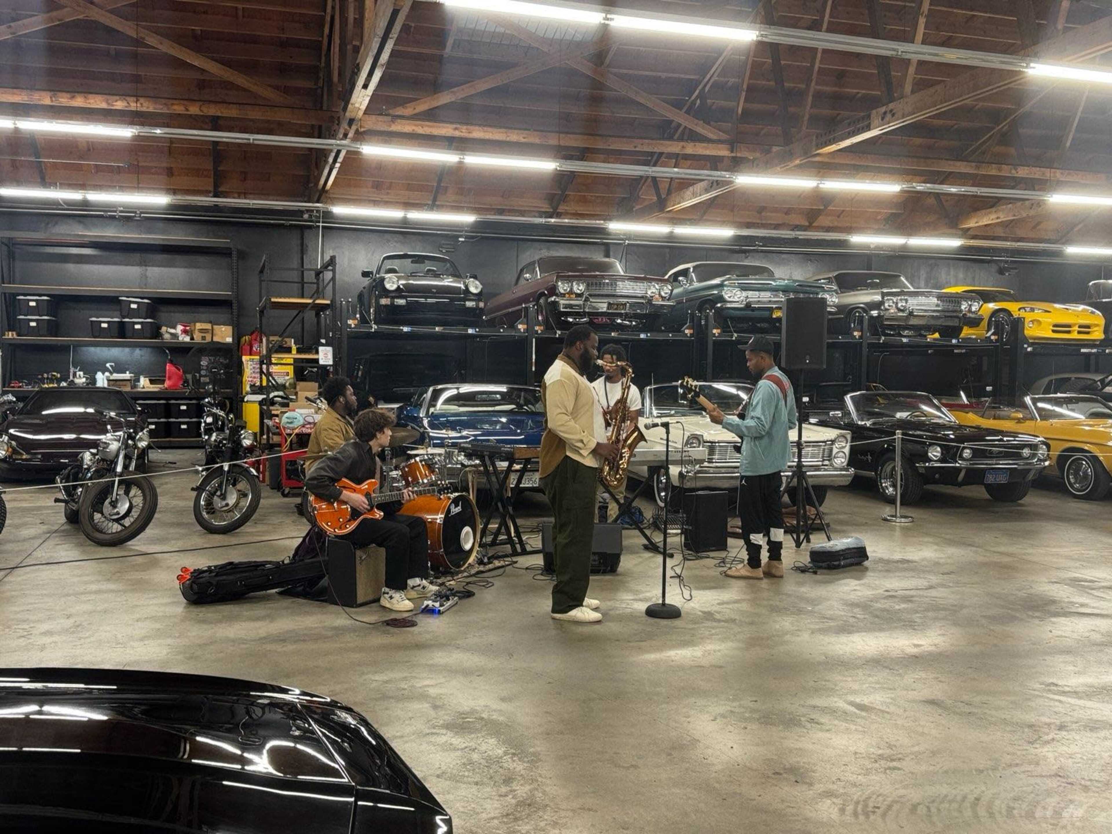 A live band performs in a garage filled with vintage cars and motorcycles.