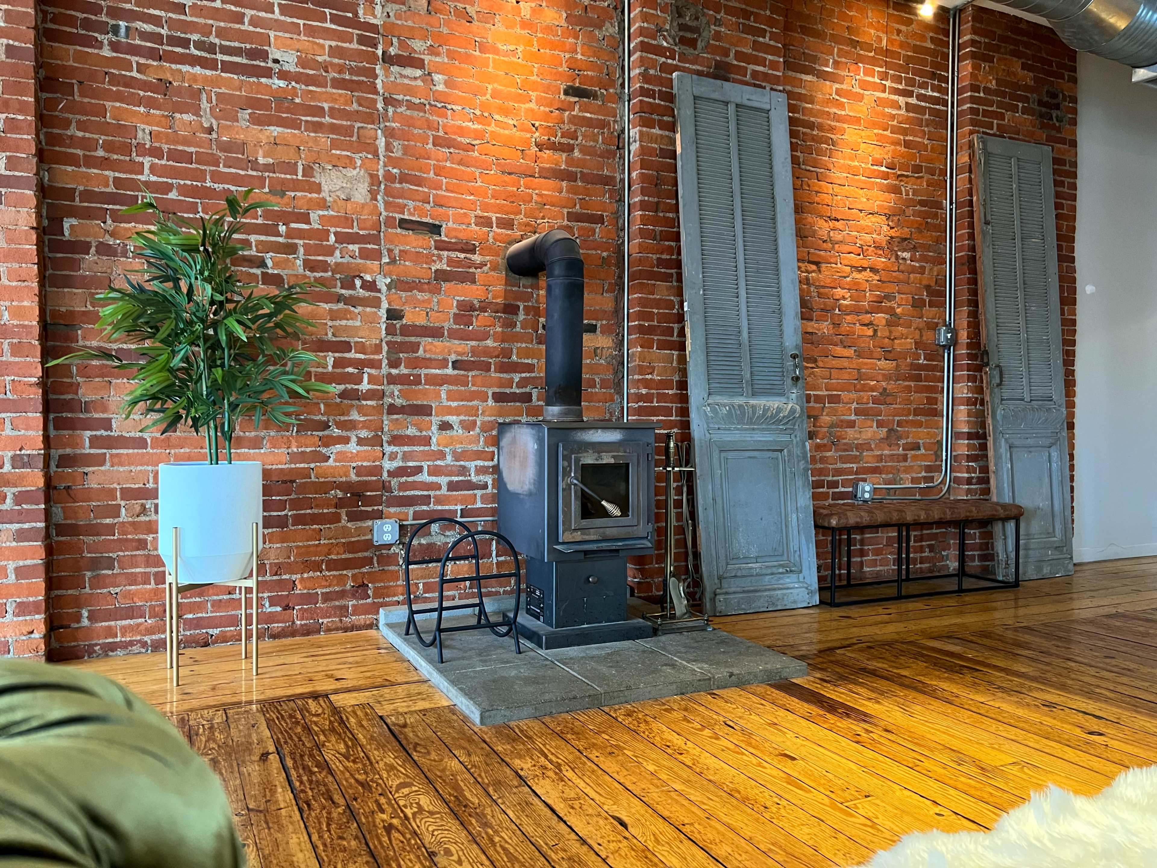 A brick wall with a black stove on a stone base, a wooden bench, and a decorative plant in a white pot.