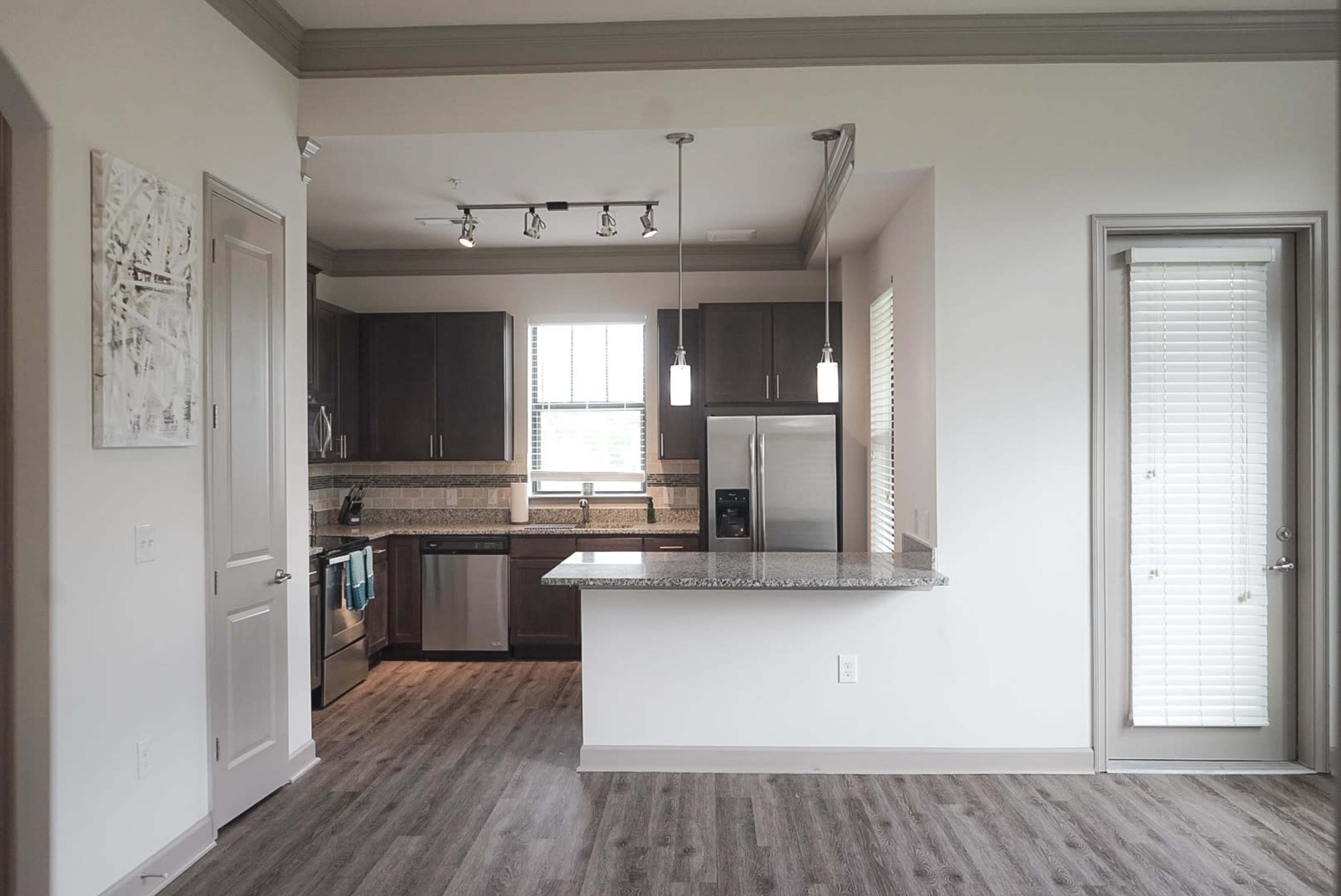 A modern kitchen with dark wood cabinets, stainless steel appliances, and a granite countertop, adjacent to a dining area with a window.