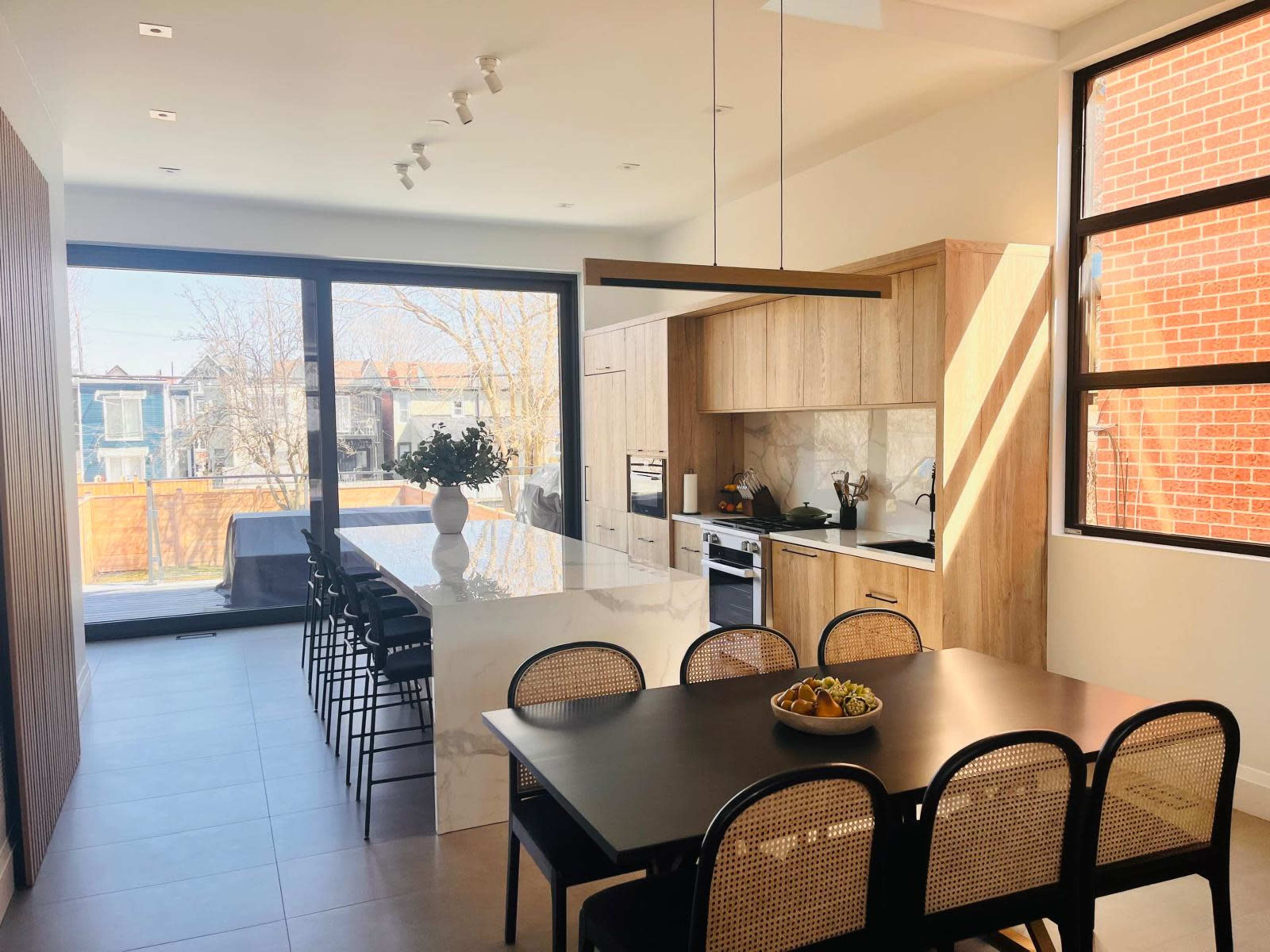The image shows a modern kitchen and dining area with an island countertop, a dining table, and large windows allowing natural light to fill the space.