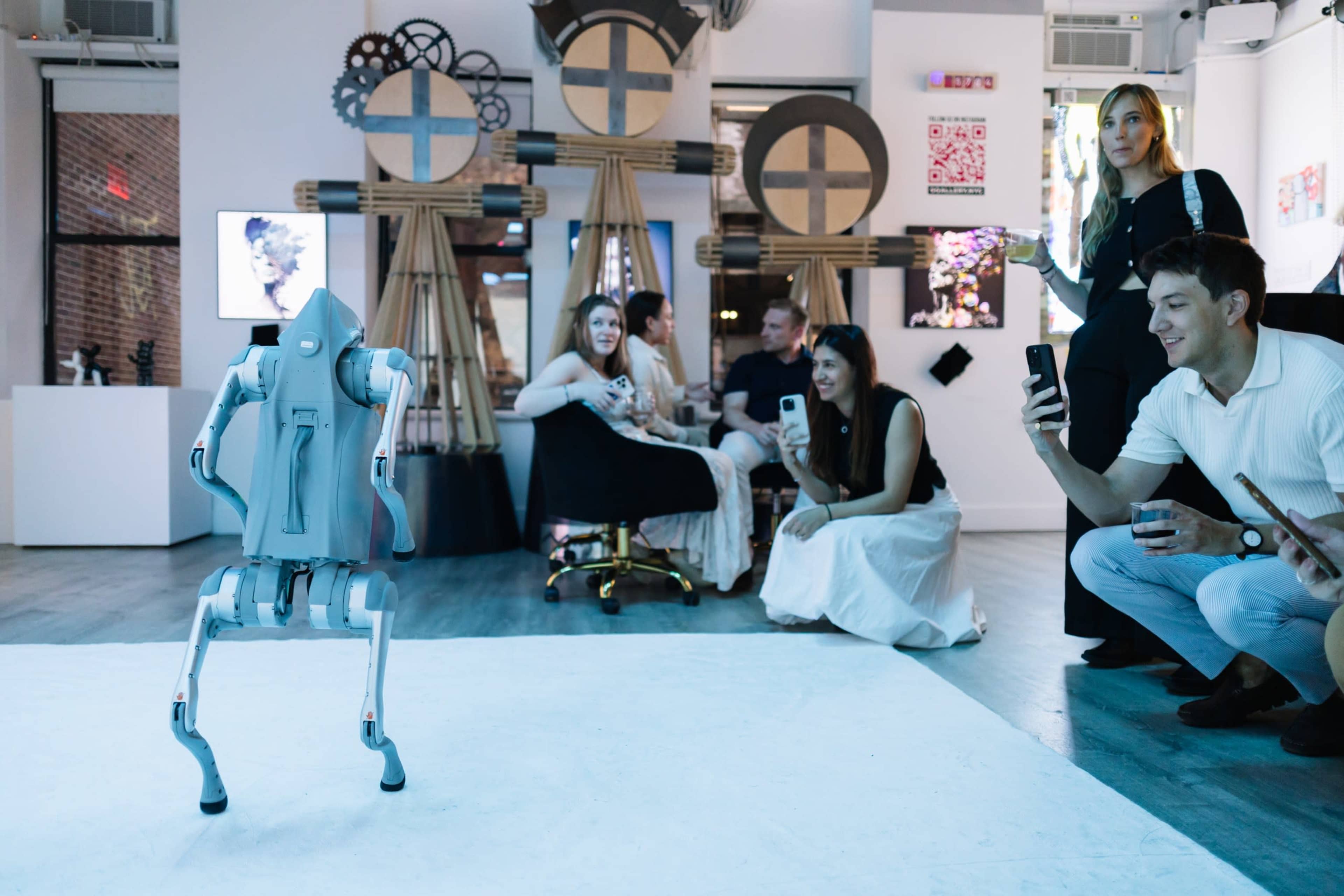 A humanoid robot performs in an art gallery while a group of people watches and takes pictures.