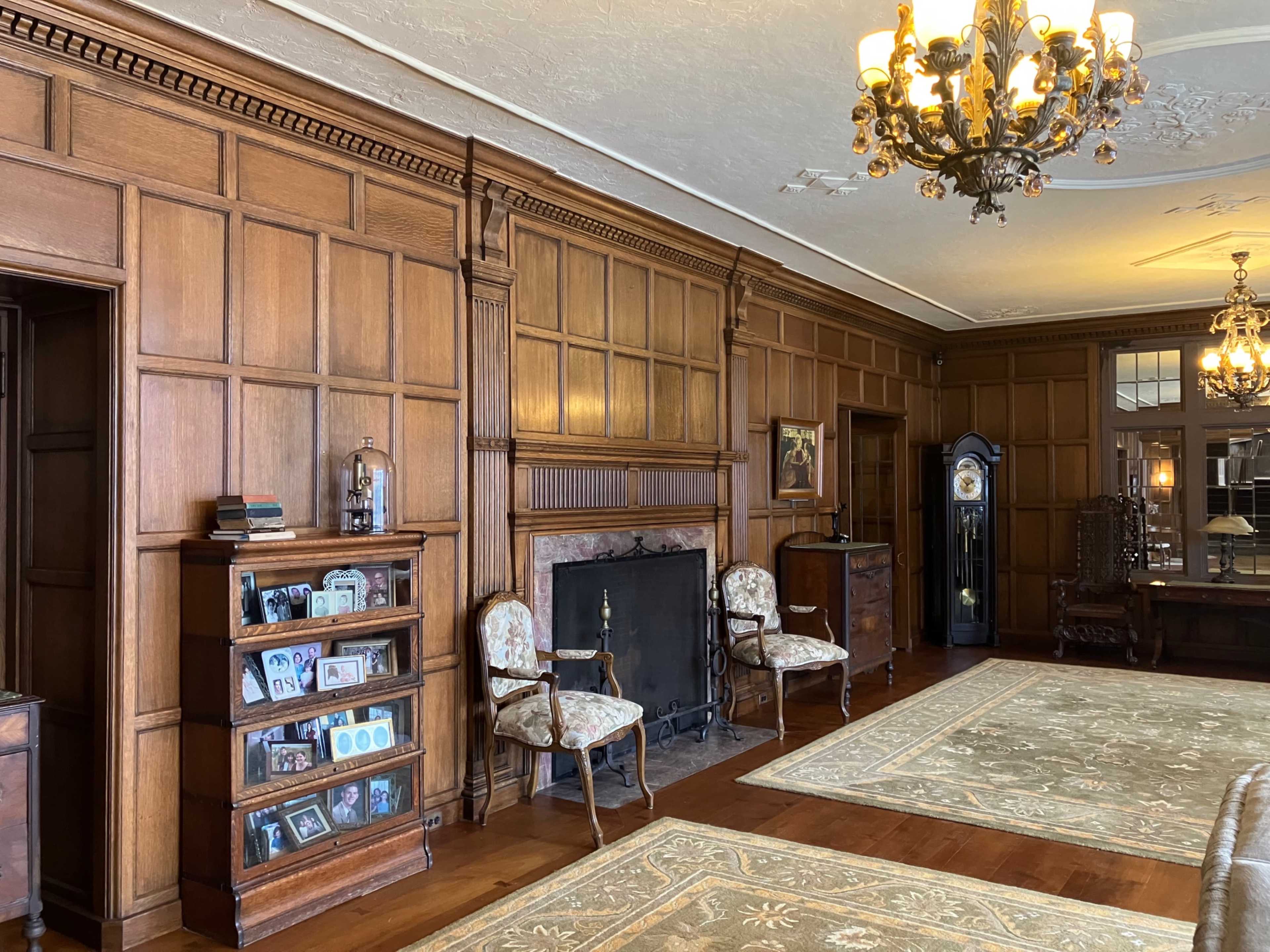 The room features wooden paneled walls, antique furniture, a fireplace, and a large area rug on the hardwood floor.