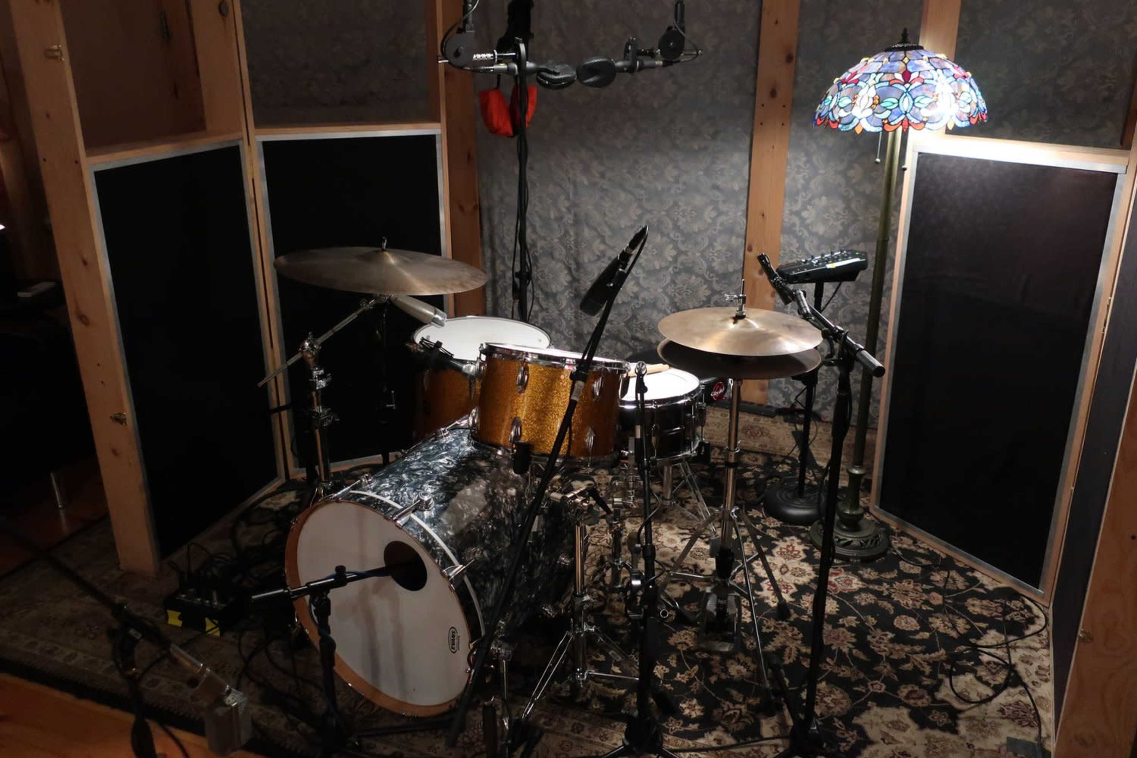 A drum set surrounded by soundproofing panels in a recording studio, with a lamp in the corner.