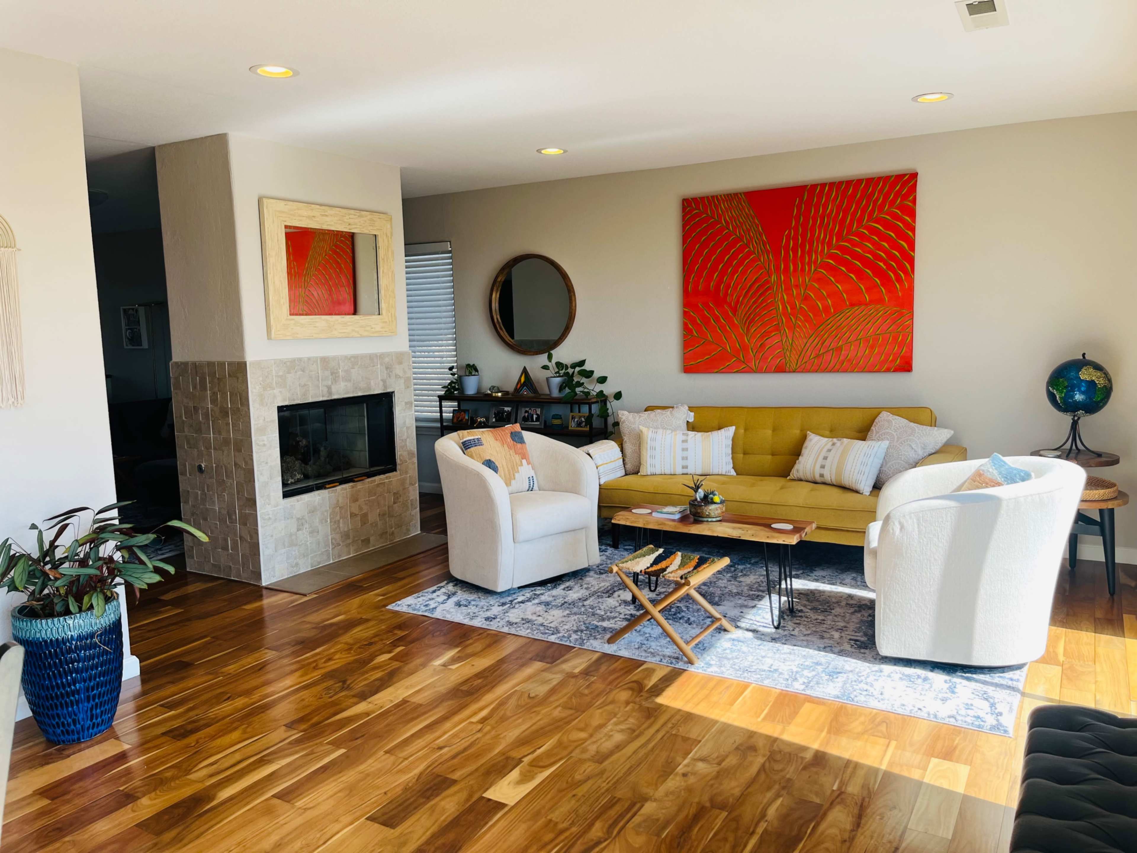 The scene features a stylish living room with a yellow sofa, two white armchairs, a fireplace, and a large orange artwork on the wall.