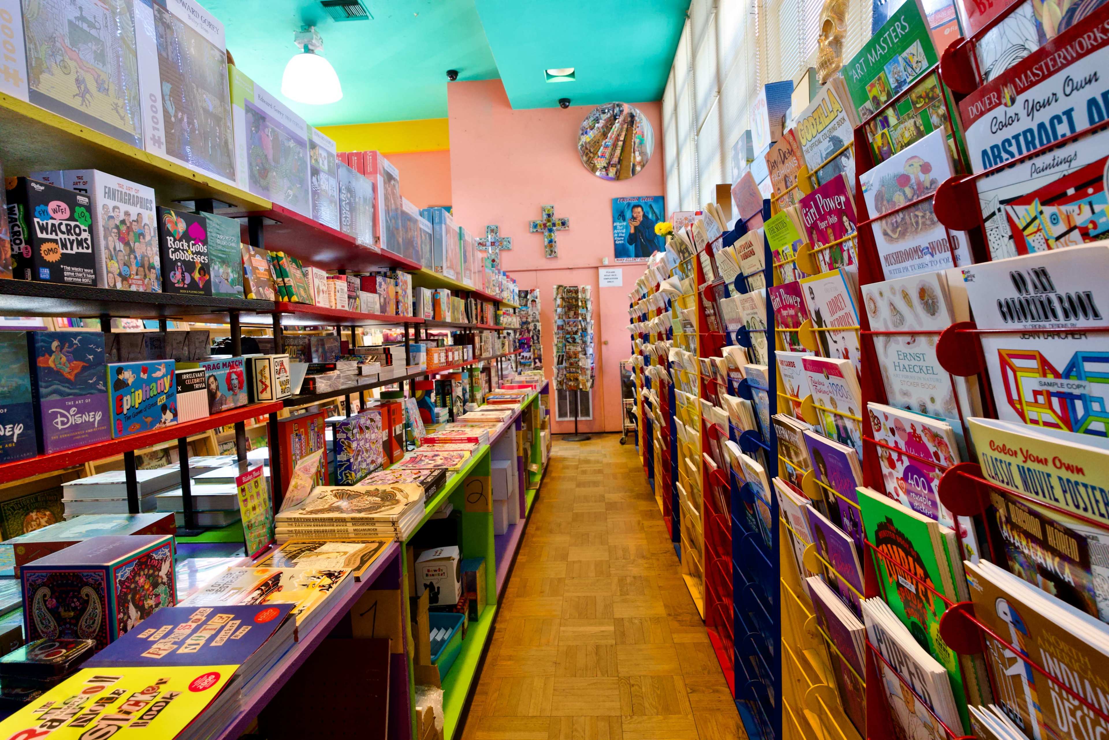 The image shows a colorful bookstore aisle lined with shelves filled with books and greeting cards.
