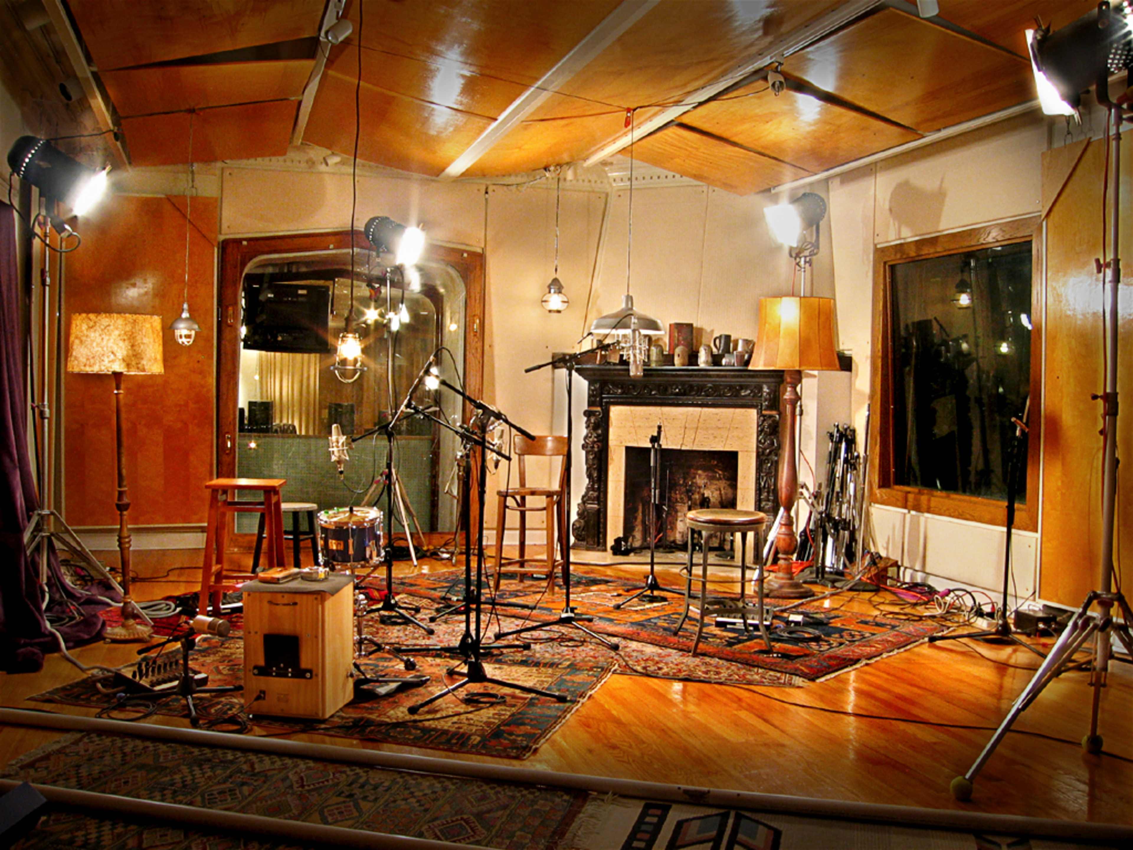 A music recording studio with several microphones, wooden chairs, and a fireplace surrounded by various instruments and warm lighting.
