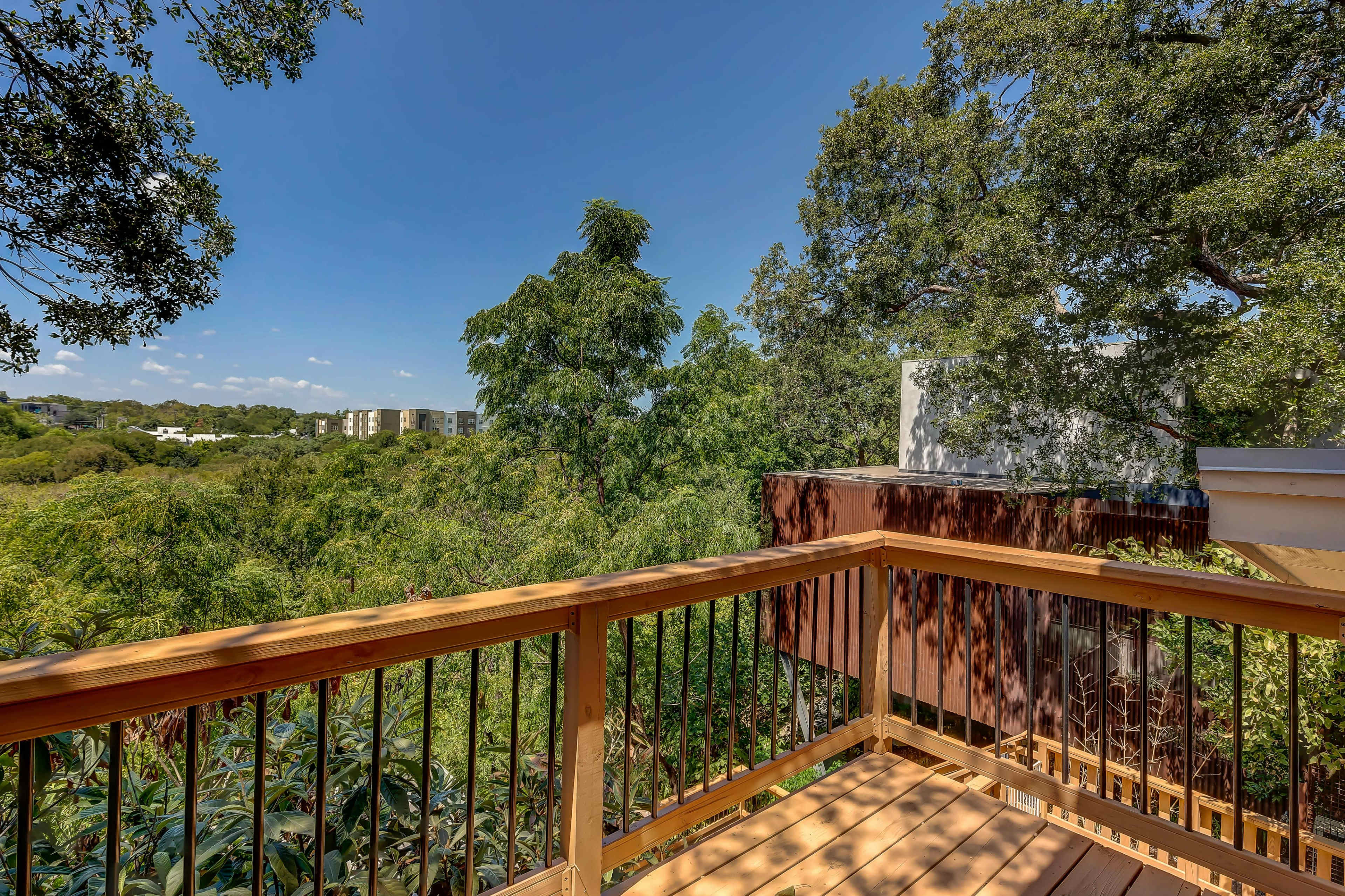 A wooden balcony overlooked a green landscape filled with trees and distant buildings under a clear blue sky.