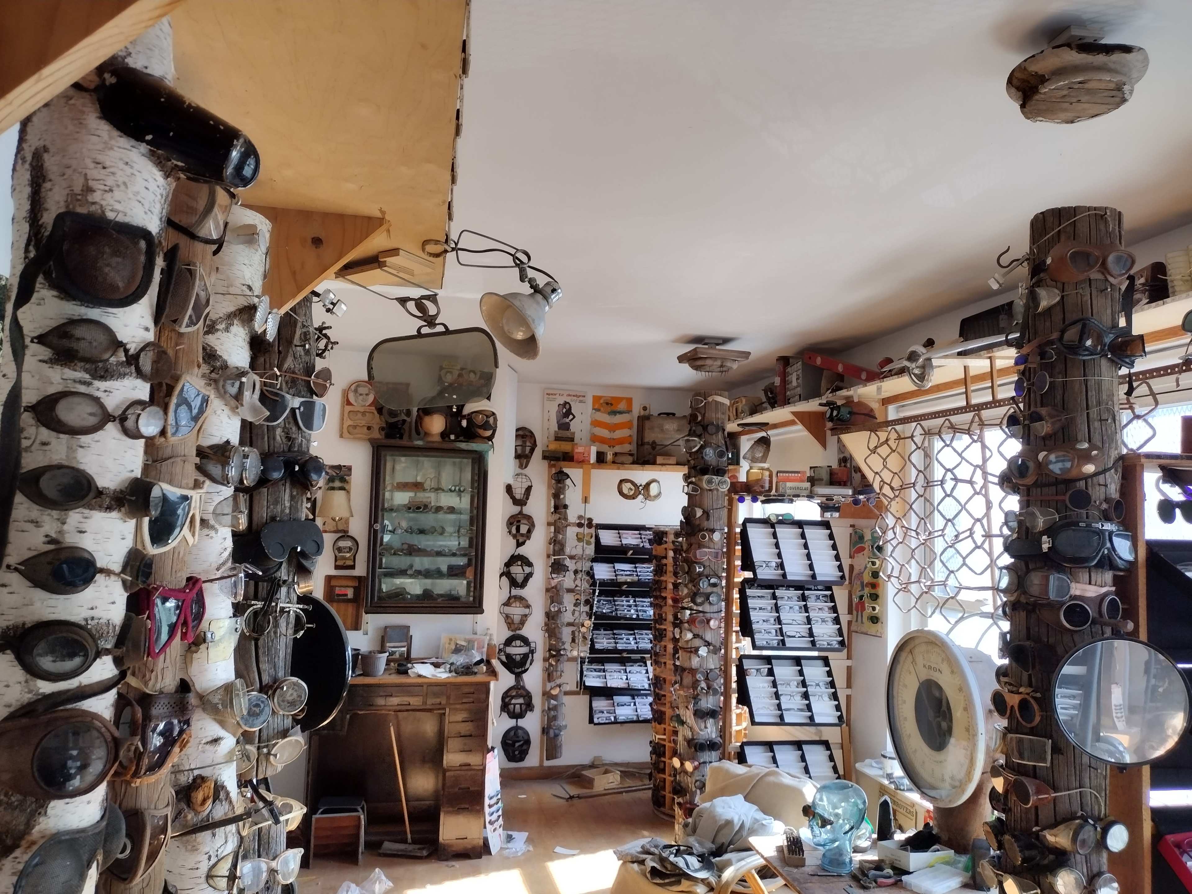 The room features wooden pillars adorned with various goggles and a wall lined with boxes, creating a cluttered yet organized workshop atmosphere.