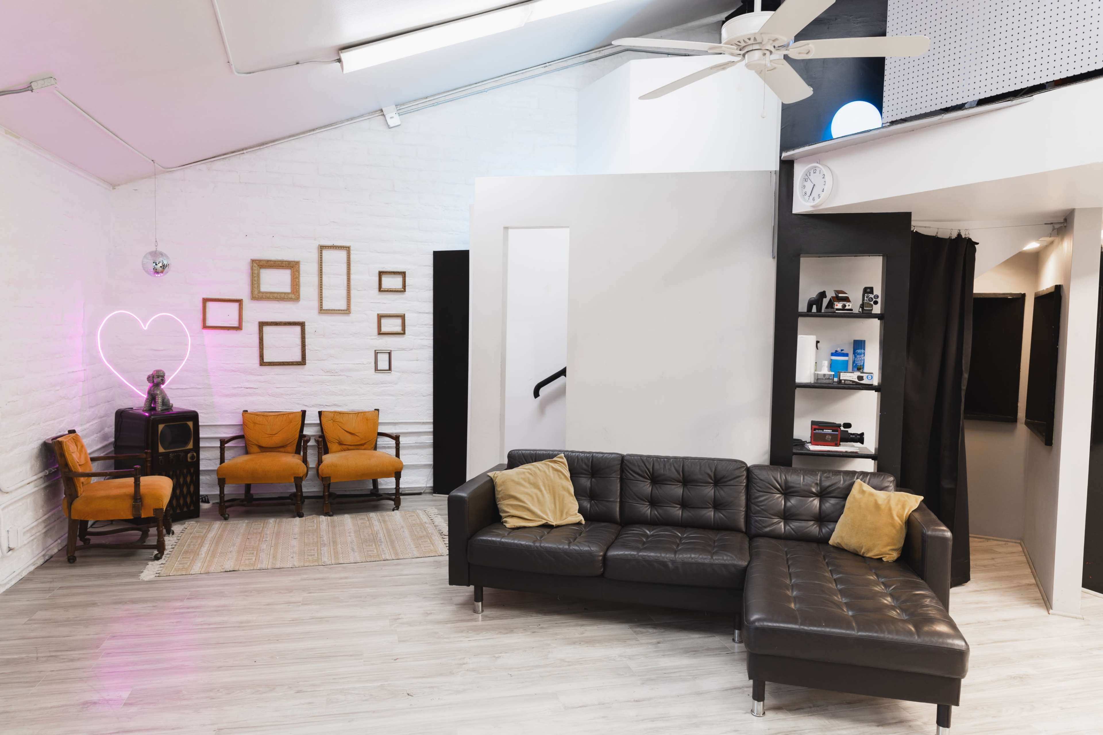A spacious interior with a black sectional sofa, a neon heart sign on the wall, and a set of orange chairs arranged around a decorative area.