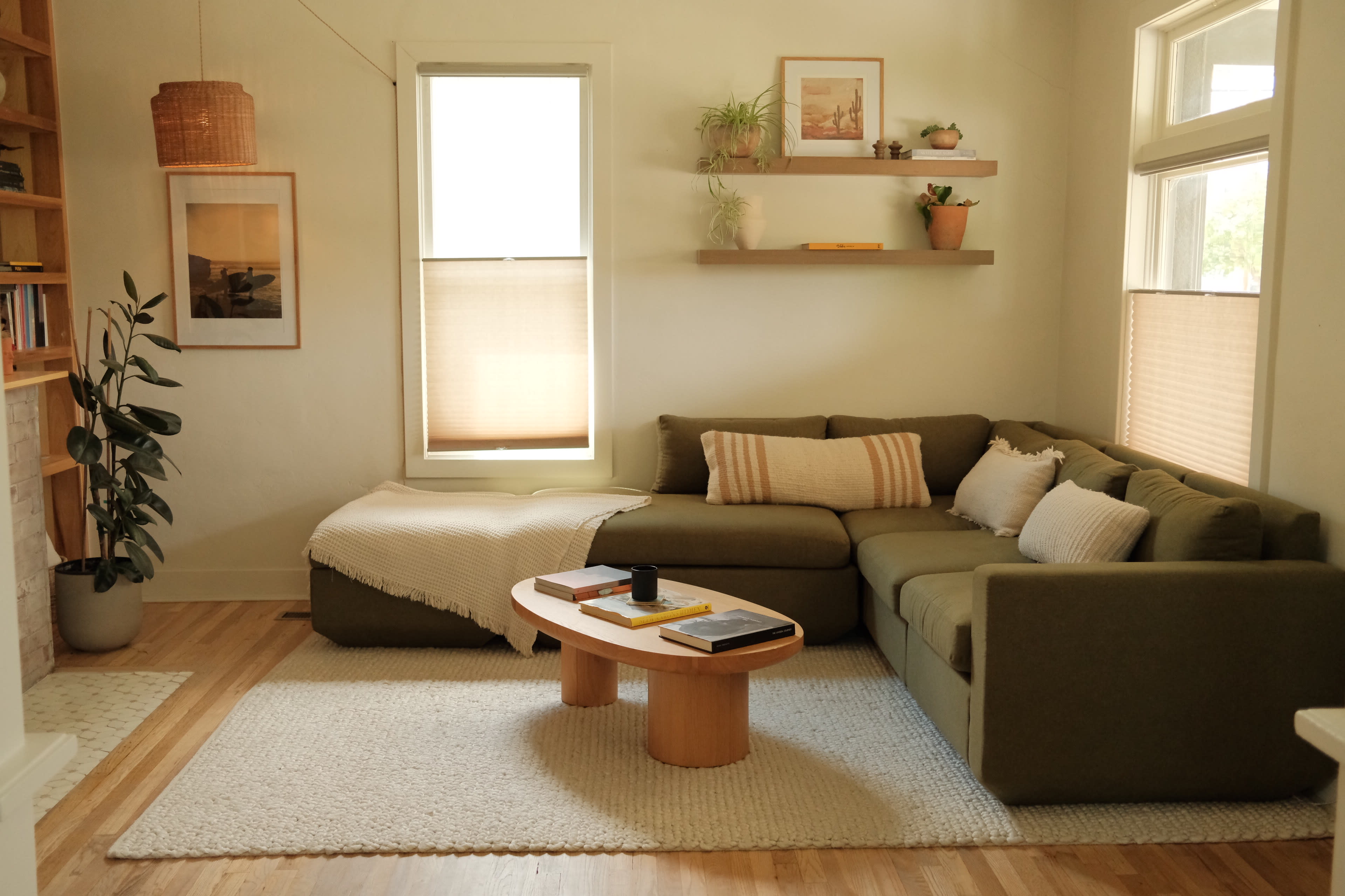 The image shows a cozy living room with a green sectional sofa, a round wooden coffee table, and minimalistic decor on the walls and shelves.