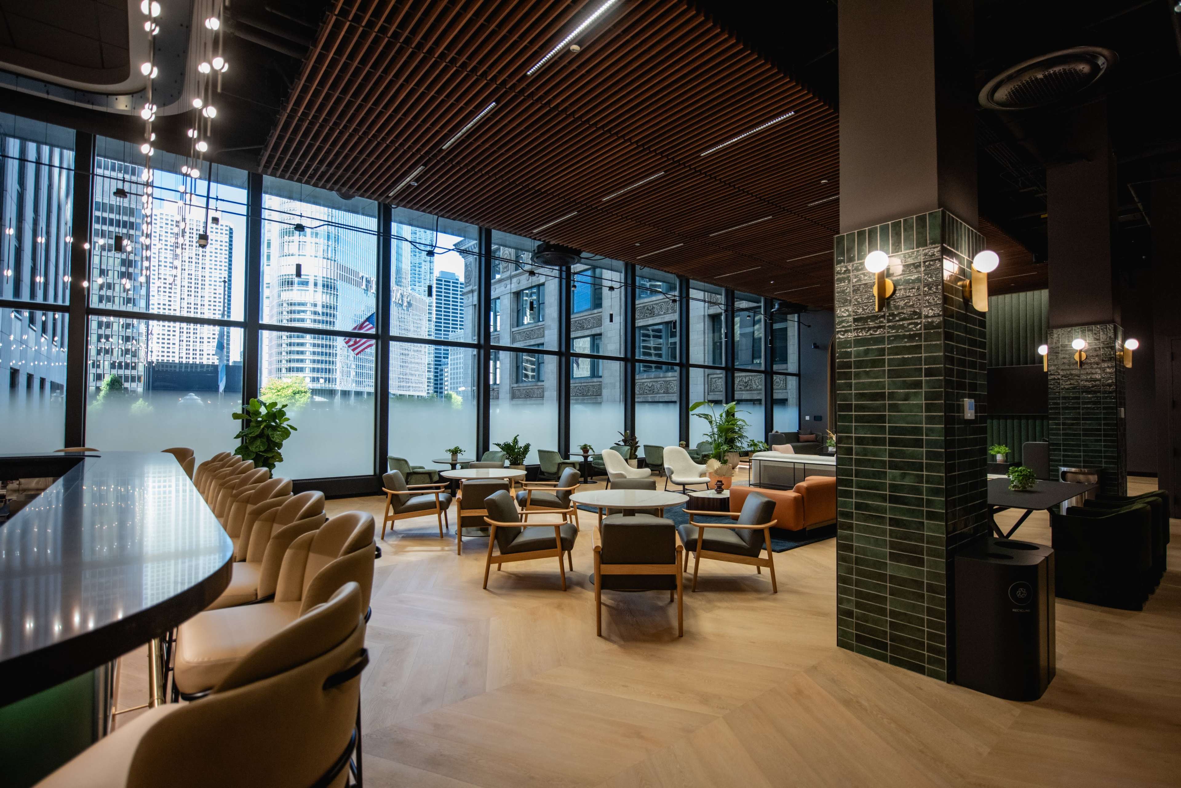 The image shows a modern café interior featuring a bar area with high chairs, various seating arrangements, and large windows overlooking a cityscape.