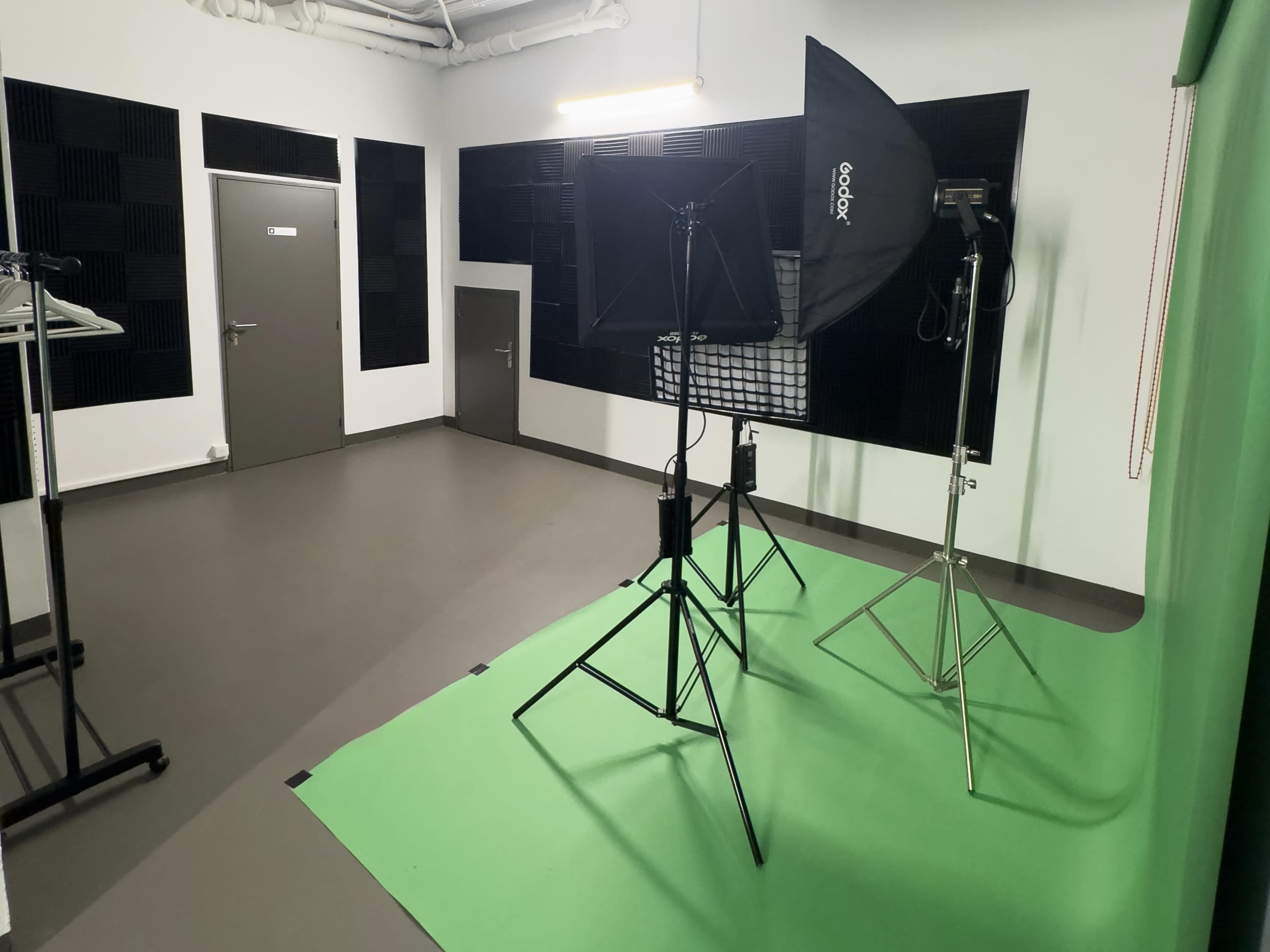 The image shows a minimalist studio space with green backdrop, lighting equipment on stands, and soundproofing panels on the walls.