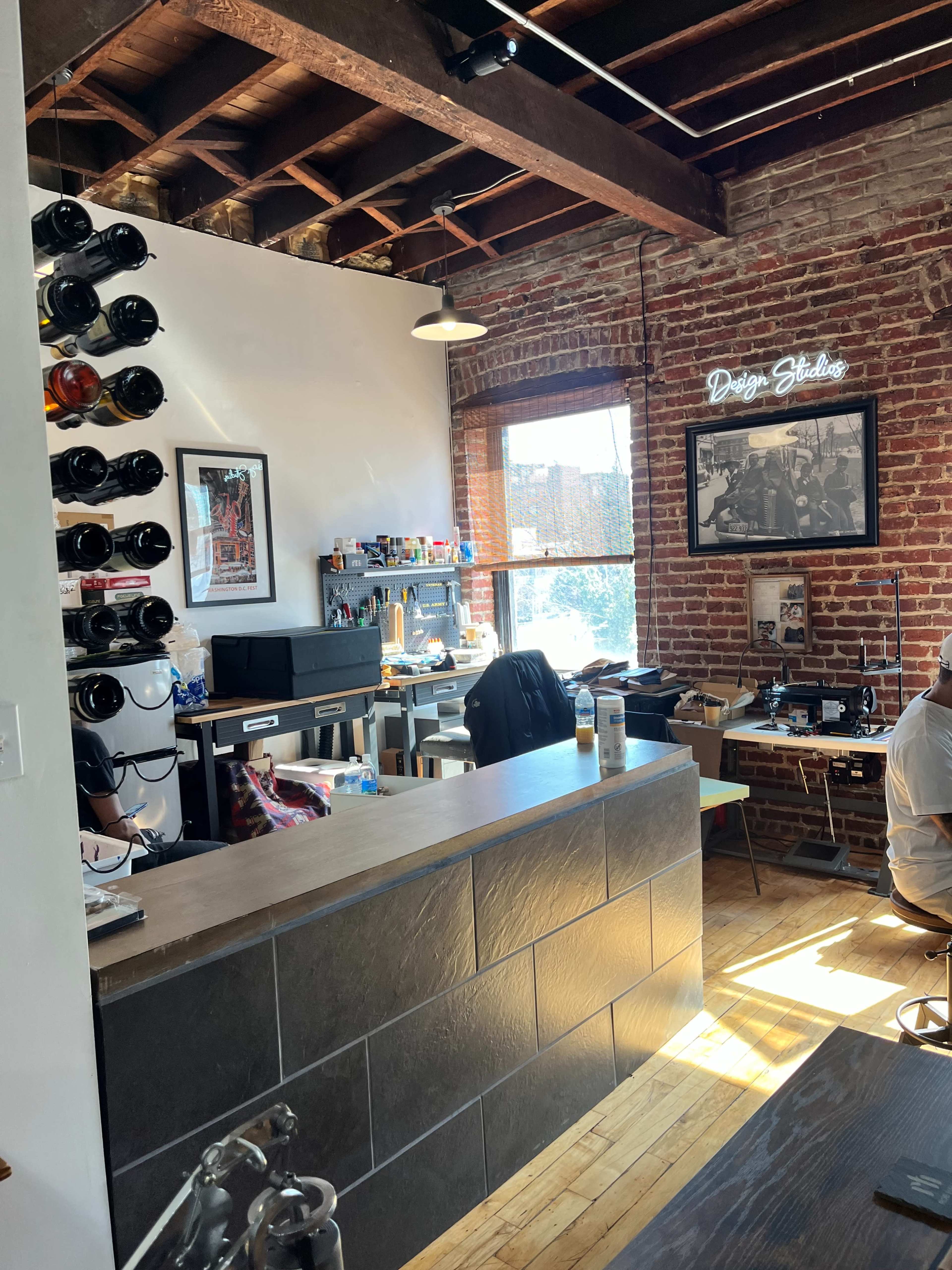 The image shows a creative workspace with exposed brick walls, a reception desk made of dark stone, and work areas cluttered with art supplies and equipment.