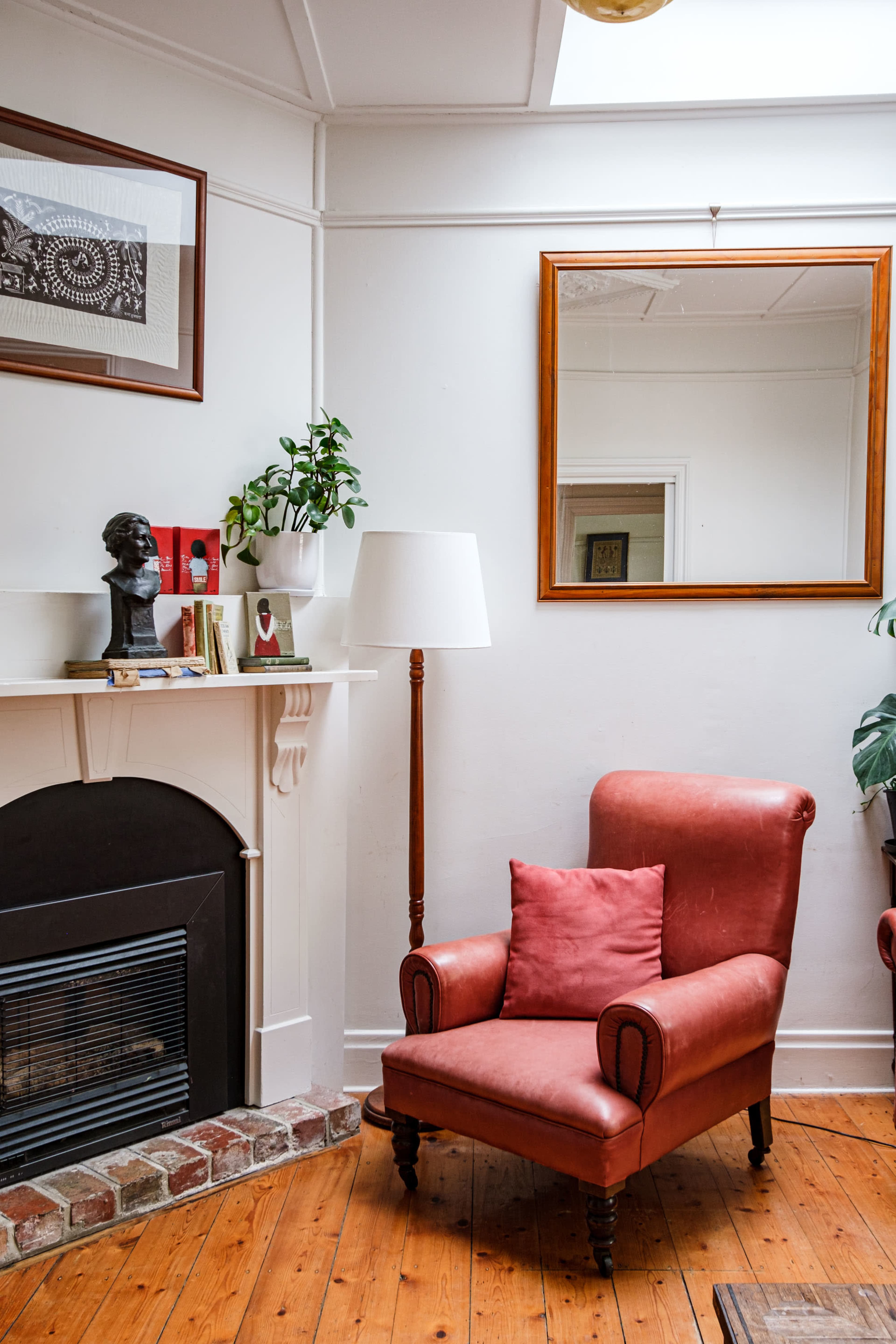 A cozy living room with a red armchair, a fireplace, a large mirror, and a plant on a shelf.