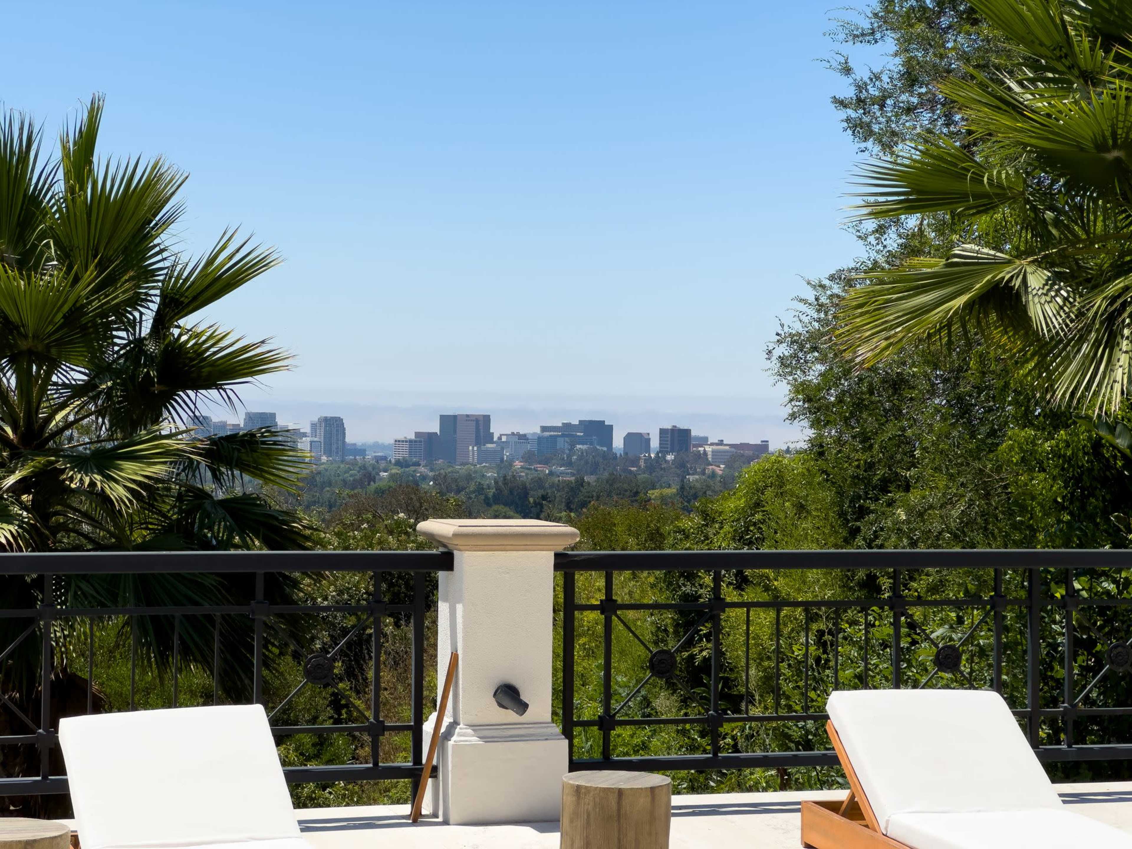 A view of a city skyline framed by palm trees and outdoor lounge chairs.