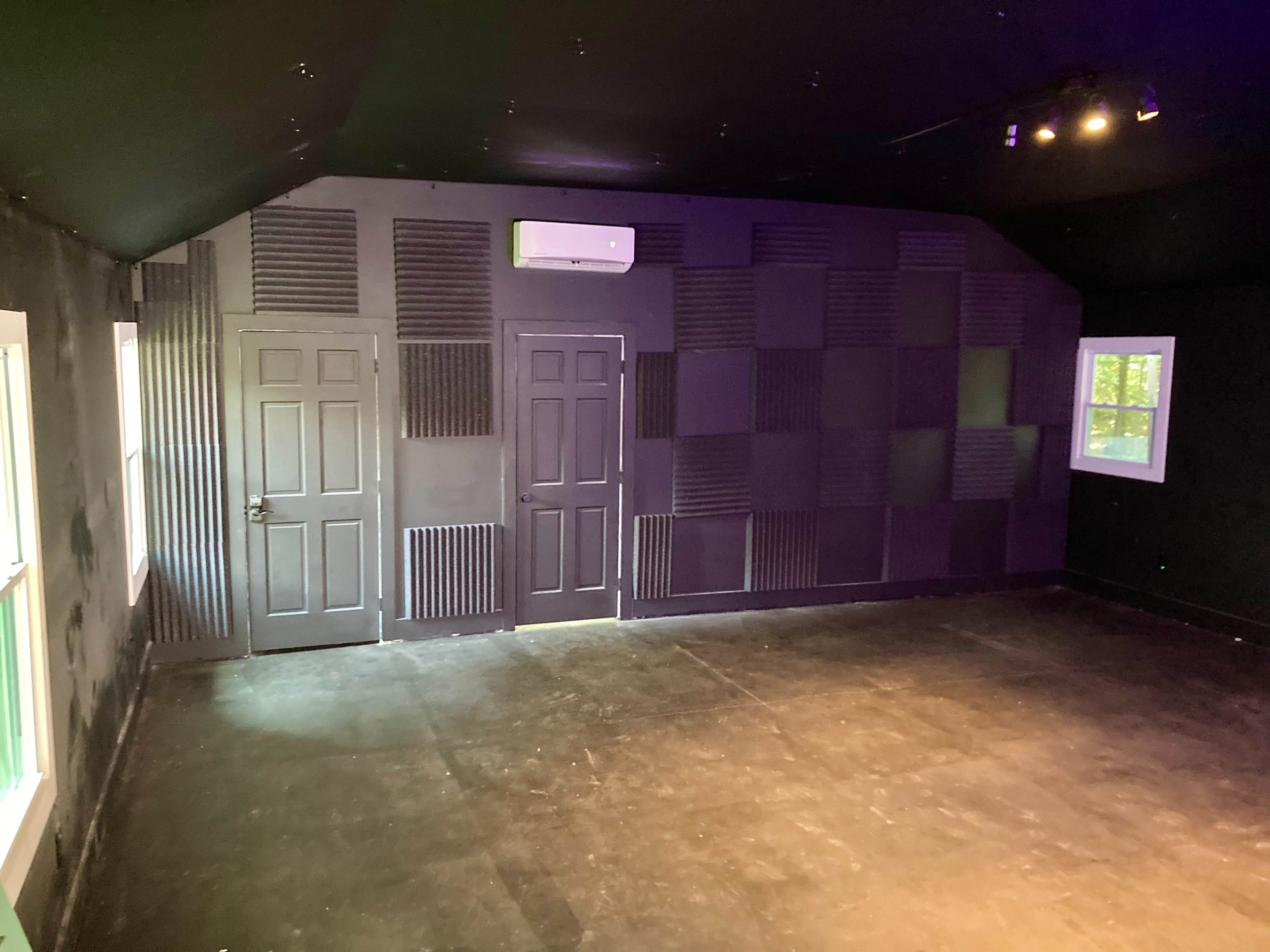 A room with black walls, two doors, and soundproofing panels on one side.
