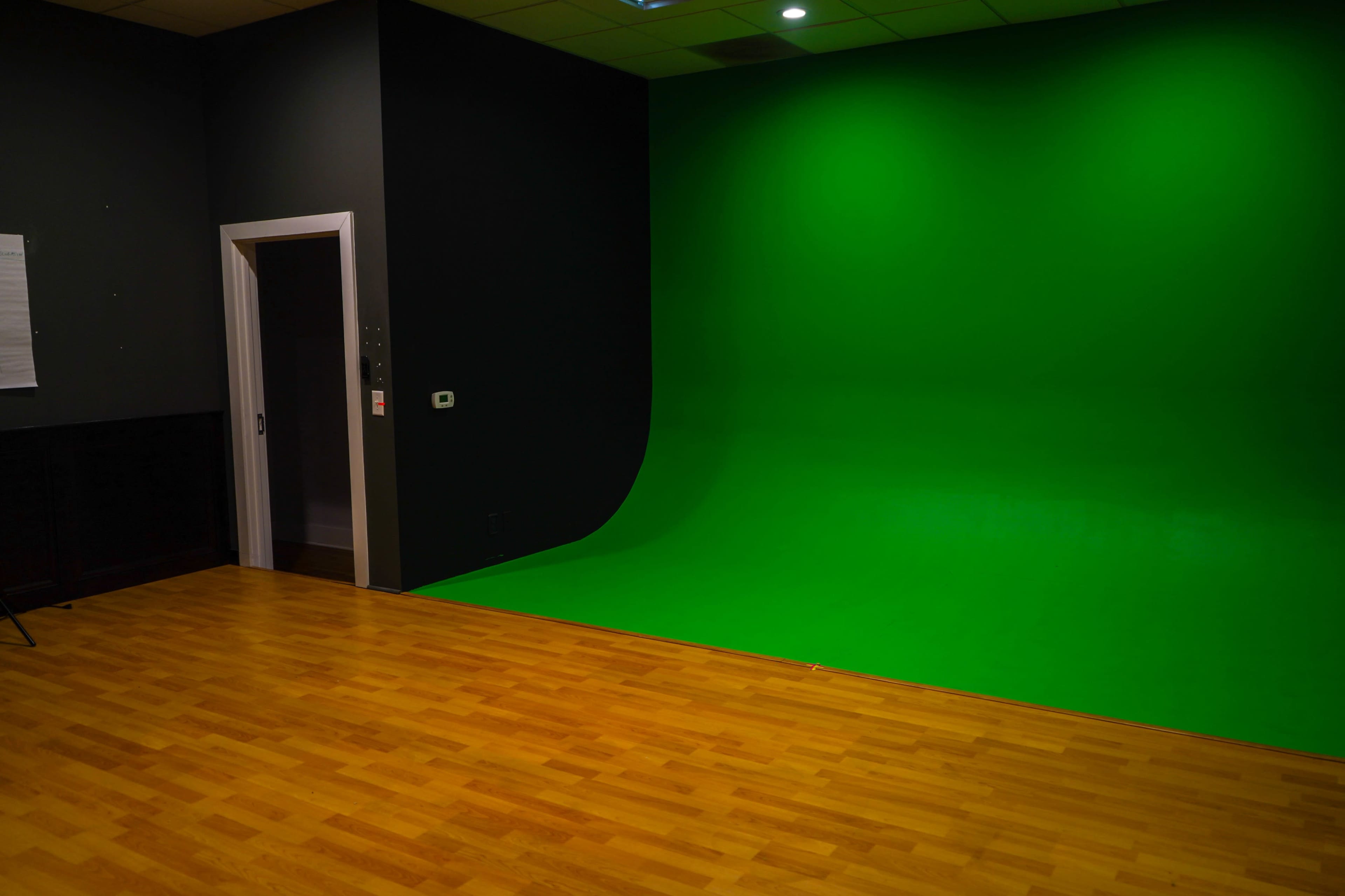 A green screen studio with a seamless green backdrop and wooden flooring.