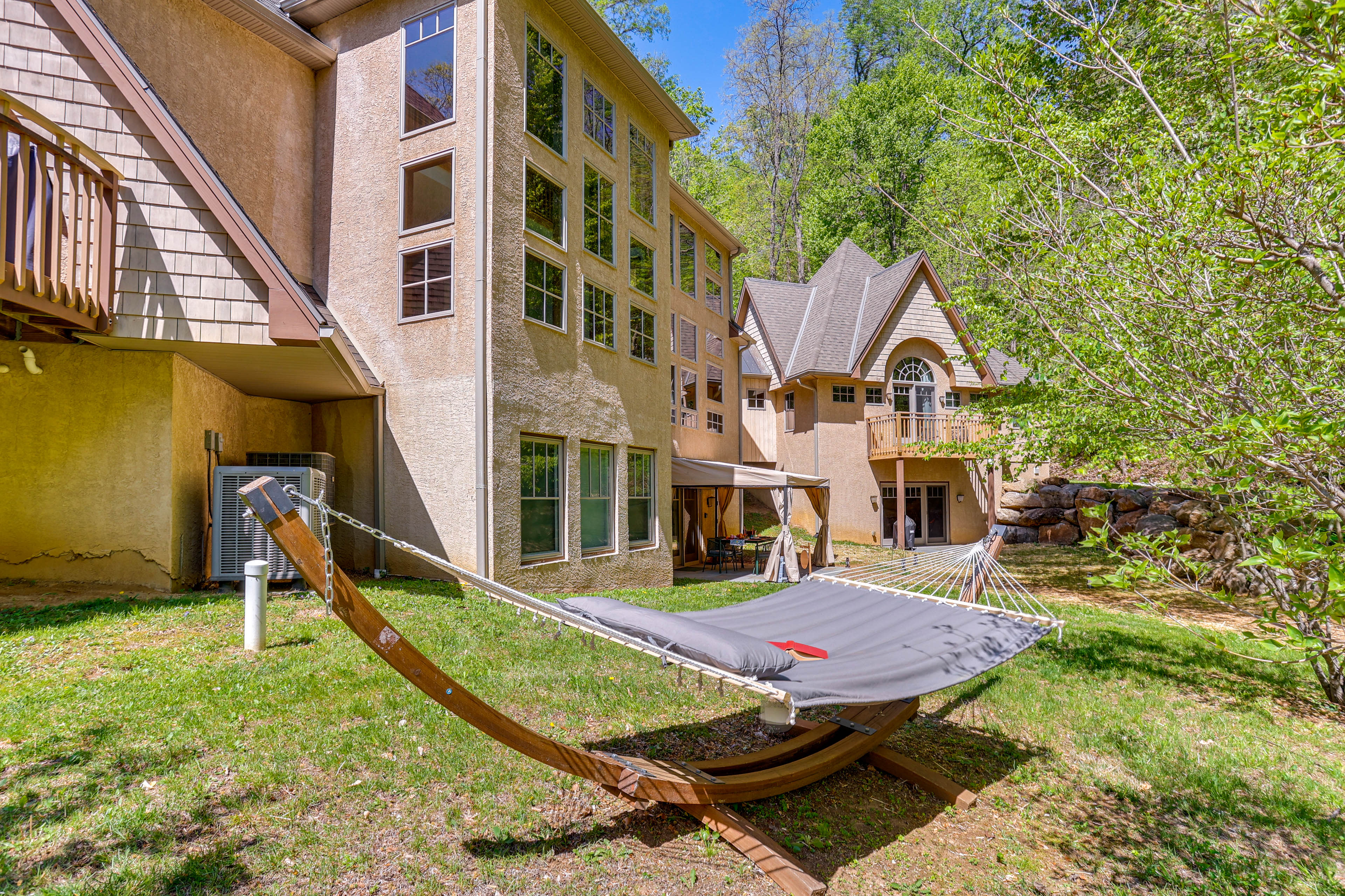 The image depicts a backyard scene featuring two large houses surrounded by greenery and a hammock set up on the lawn.