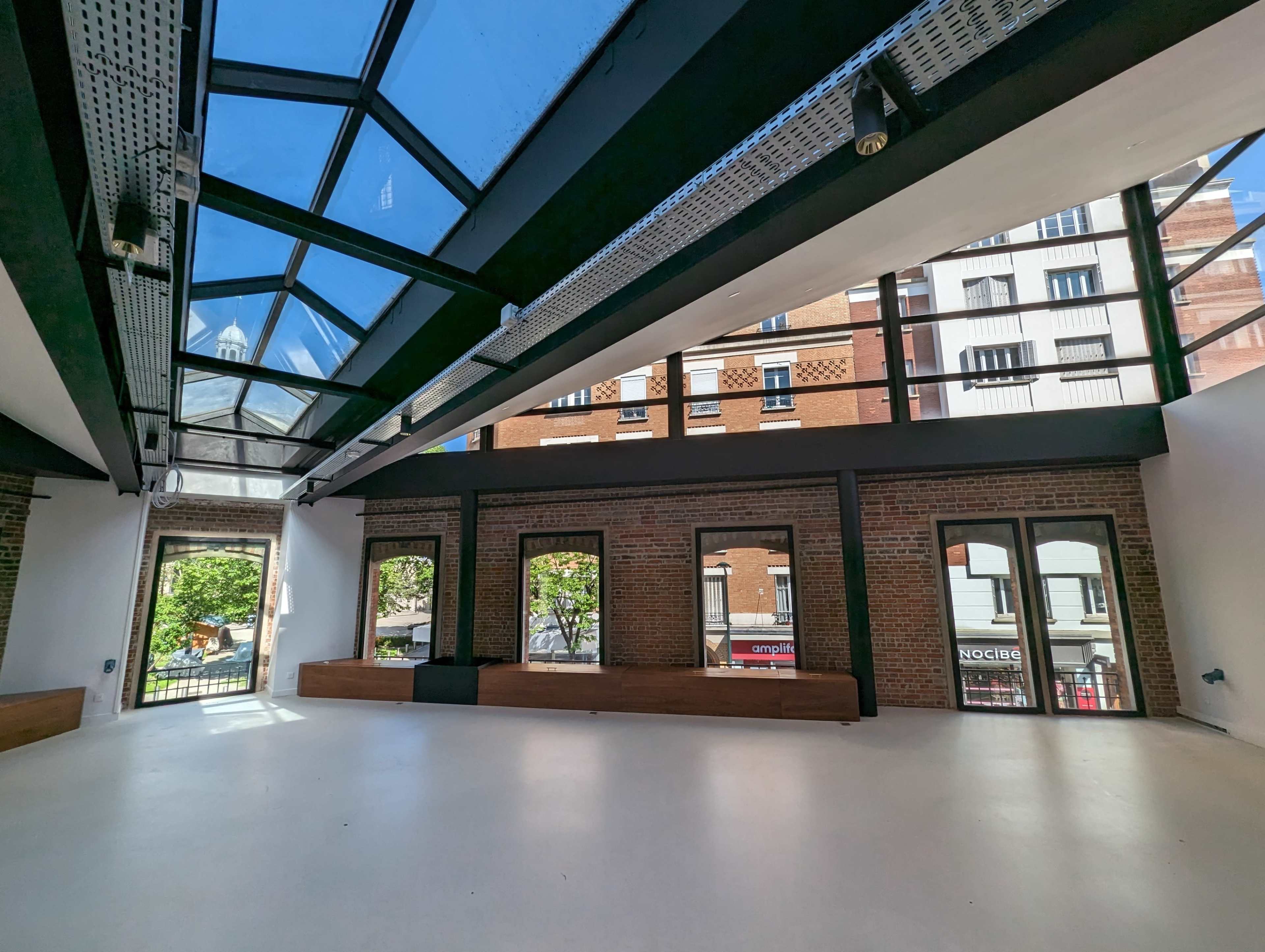 A spacious interior with large windows and a skylight, featuring exposed brick walls and a light-colored floor.