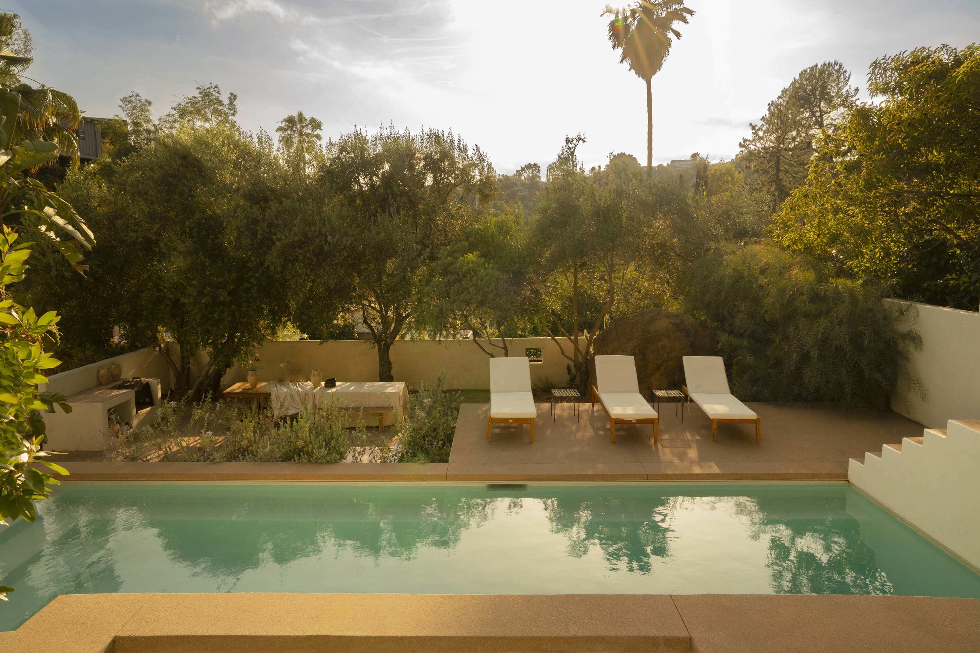 A serene outdoor pool area surrounded by greenery and sun loungers under a clear sky.