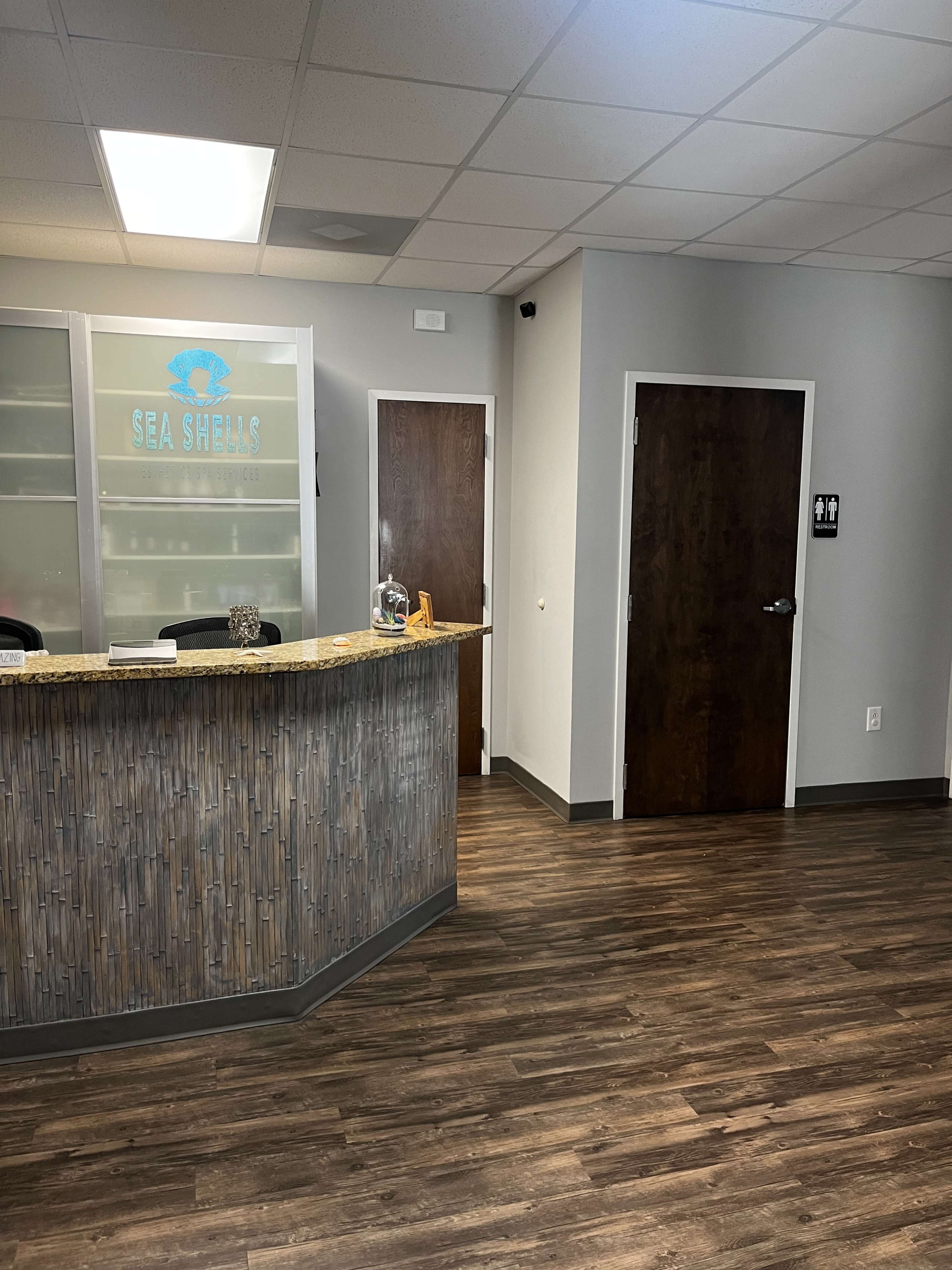 A modern reception area with a curved counter, glass partitions, and a door labeled with restroom symbols.