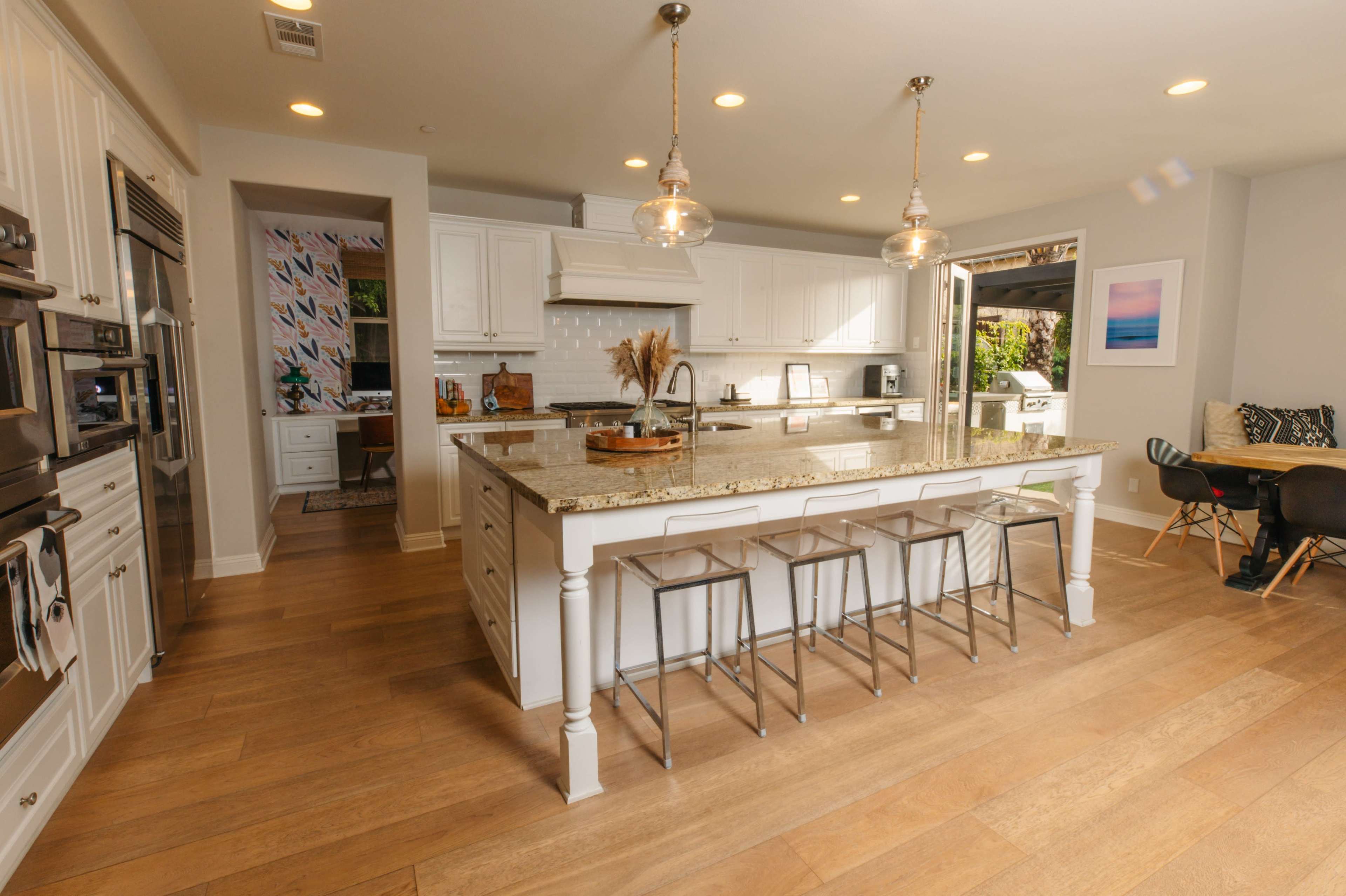 A modern kitchen features white cabinetry, a large island with seating, and an open layout leading to an outdoor area.