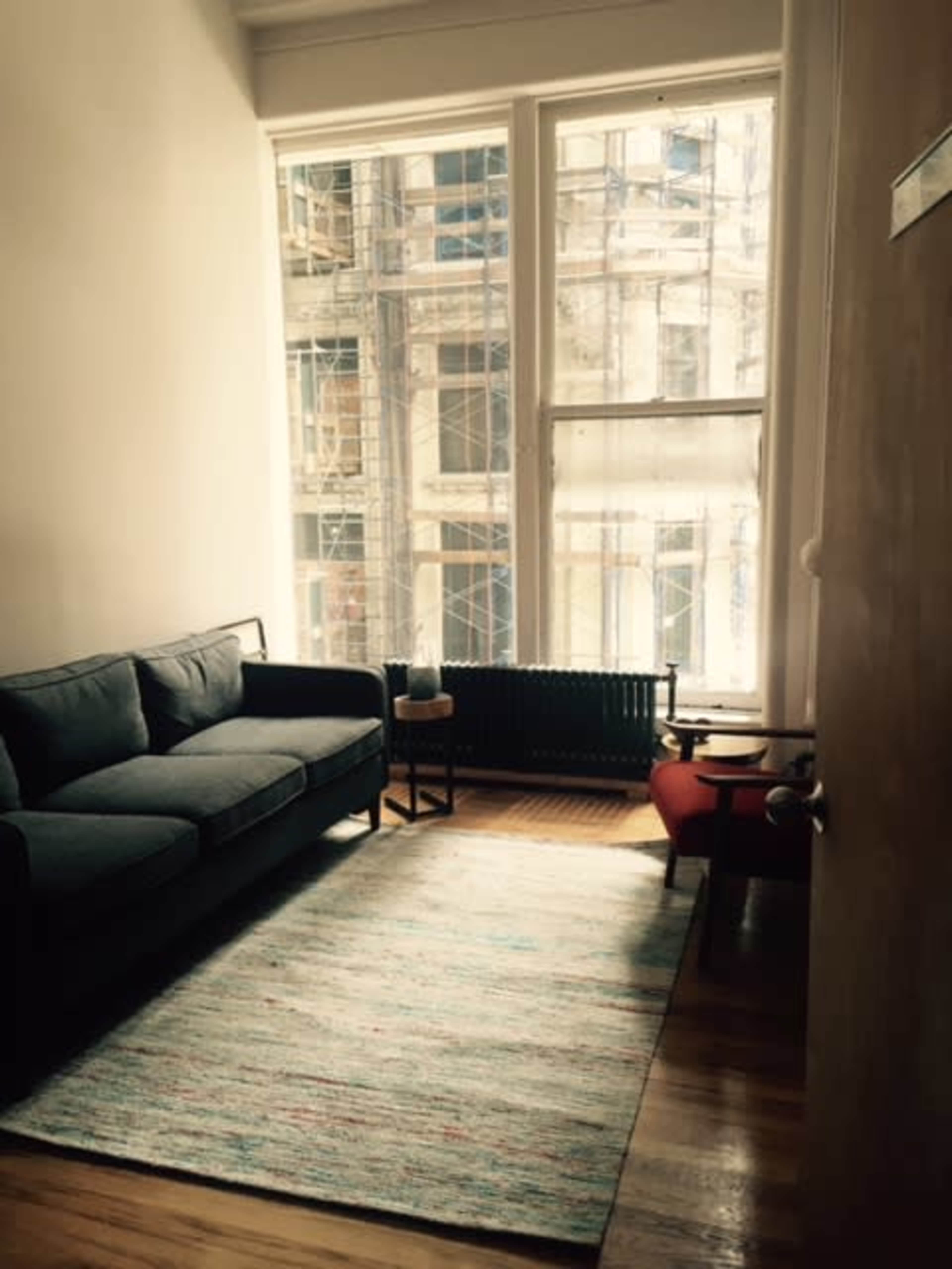 A small living room features a couch, a rug, and large windows overlooking a cityscape.