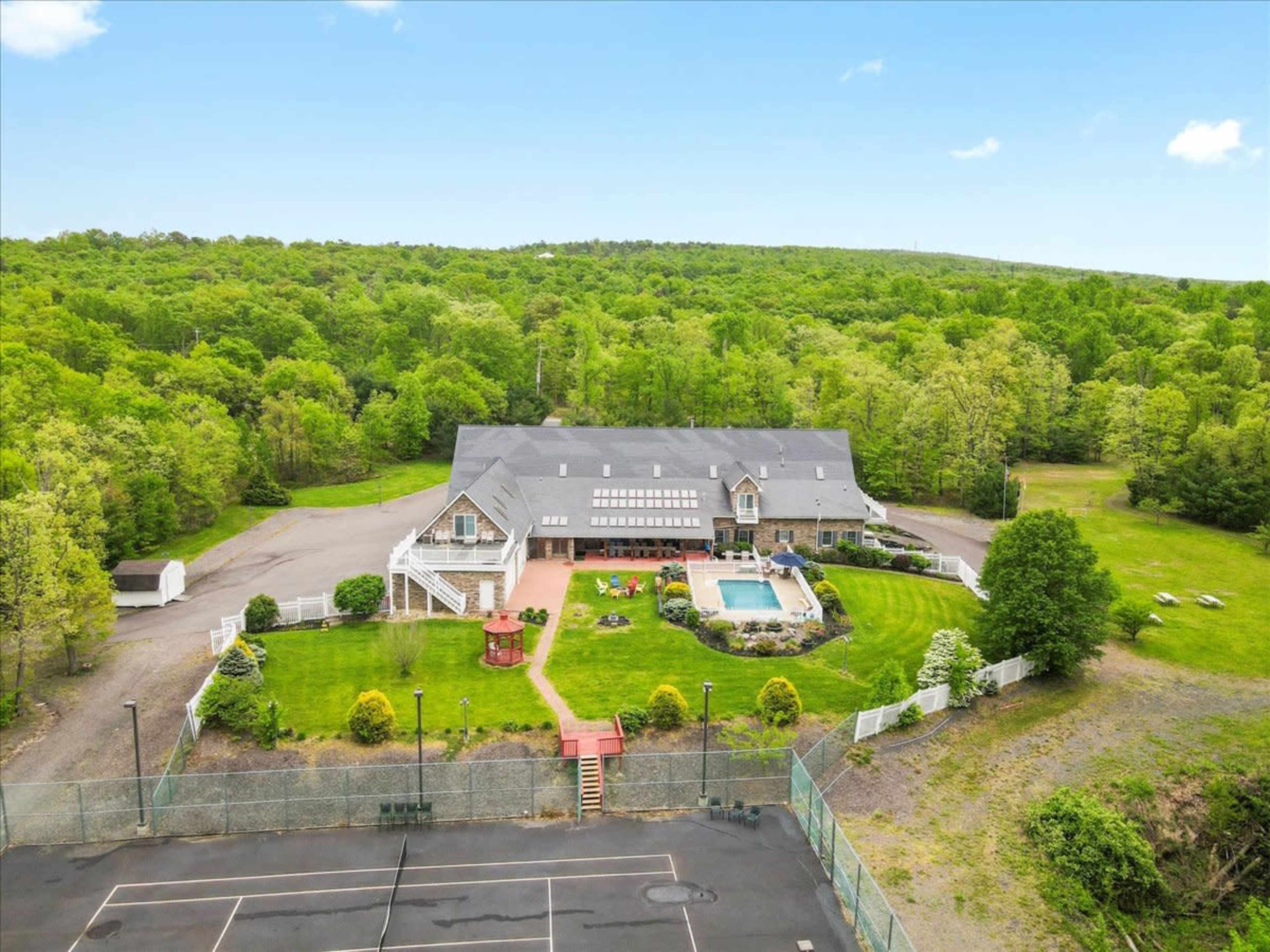 A large mansion surrounded by lush greenery features a swimming pool, tennis court, and well-maintained gardens.