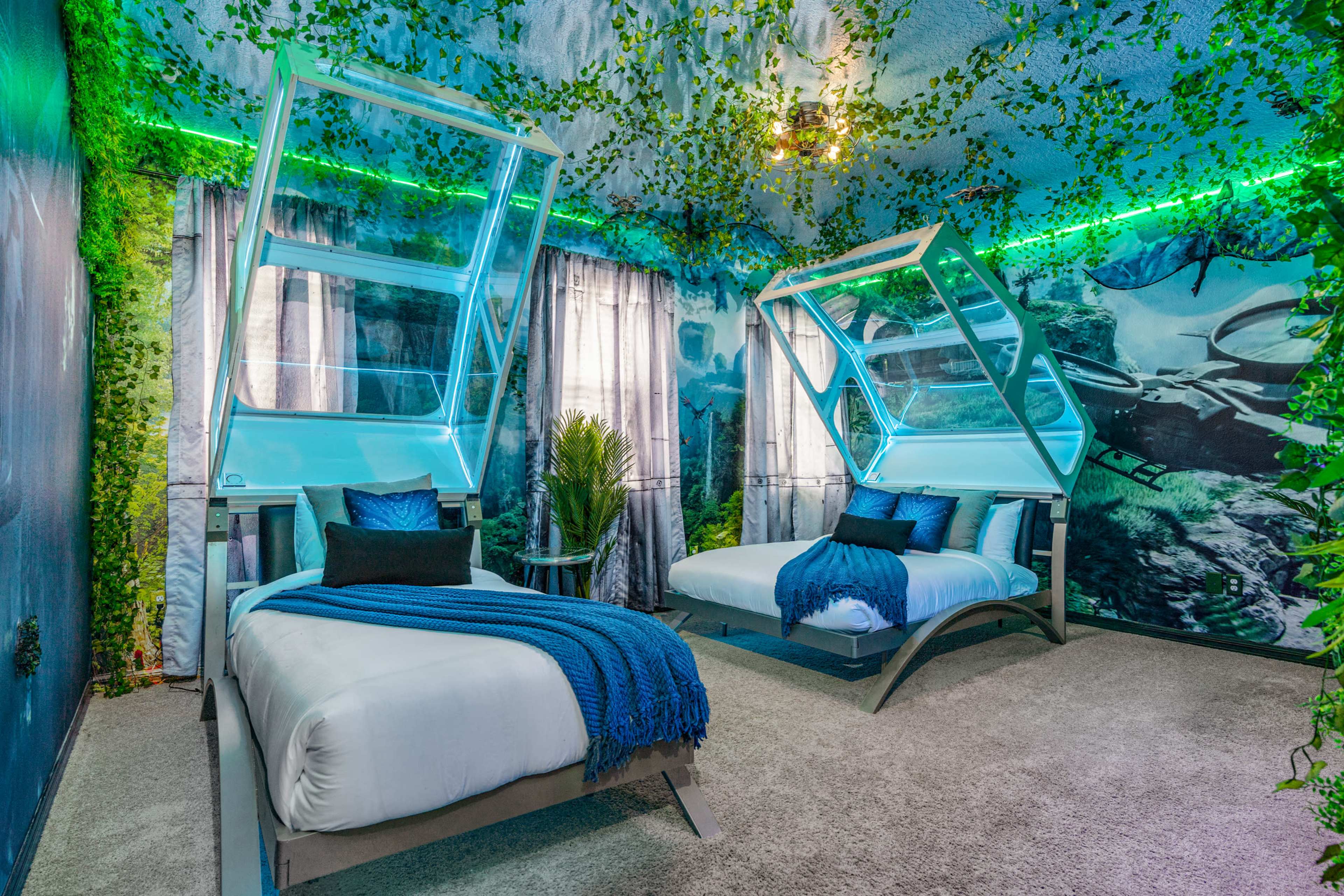 The room features two beds with raised frames, surrounded by walls decorated with a forest mural and lush green foliage.