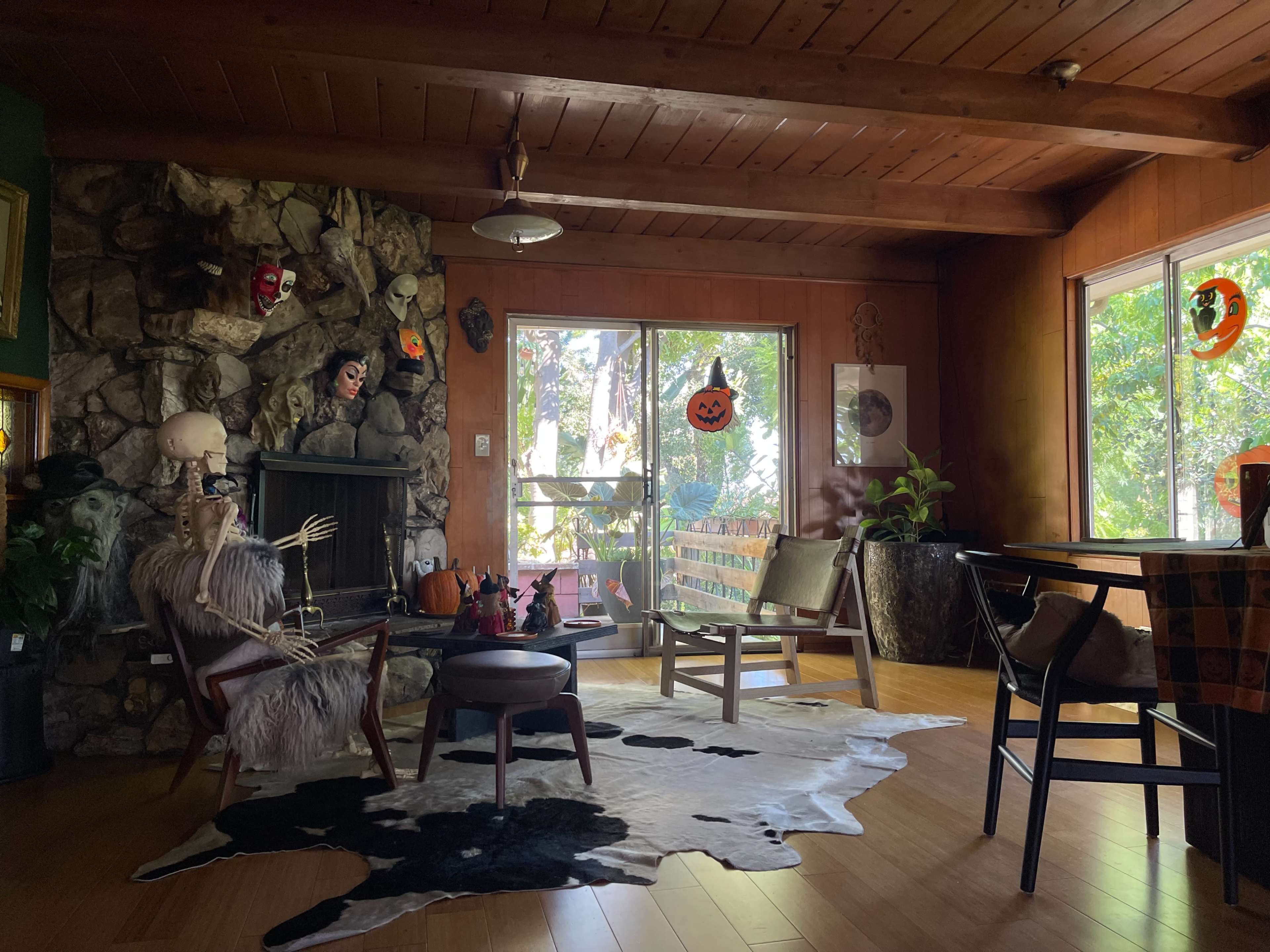 The room features a rustic stone fireplace, a skeleton decoratively posed on a chair, and Halloween-themed decorations on the walls and window.