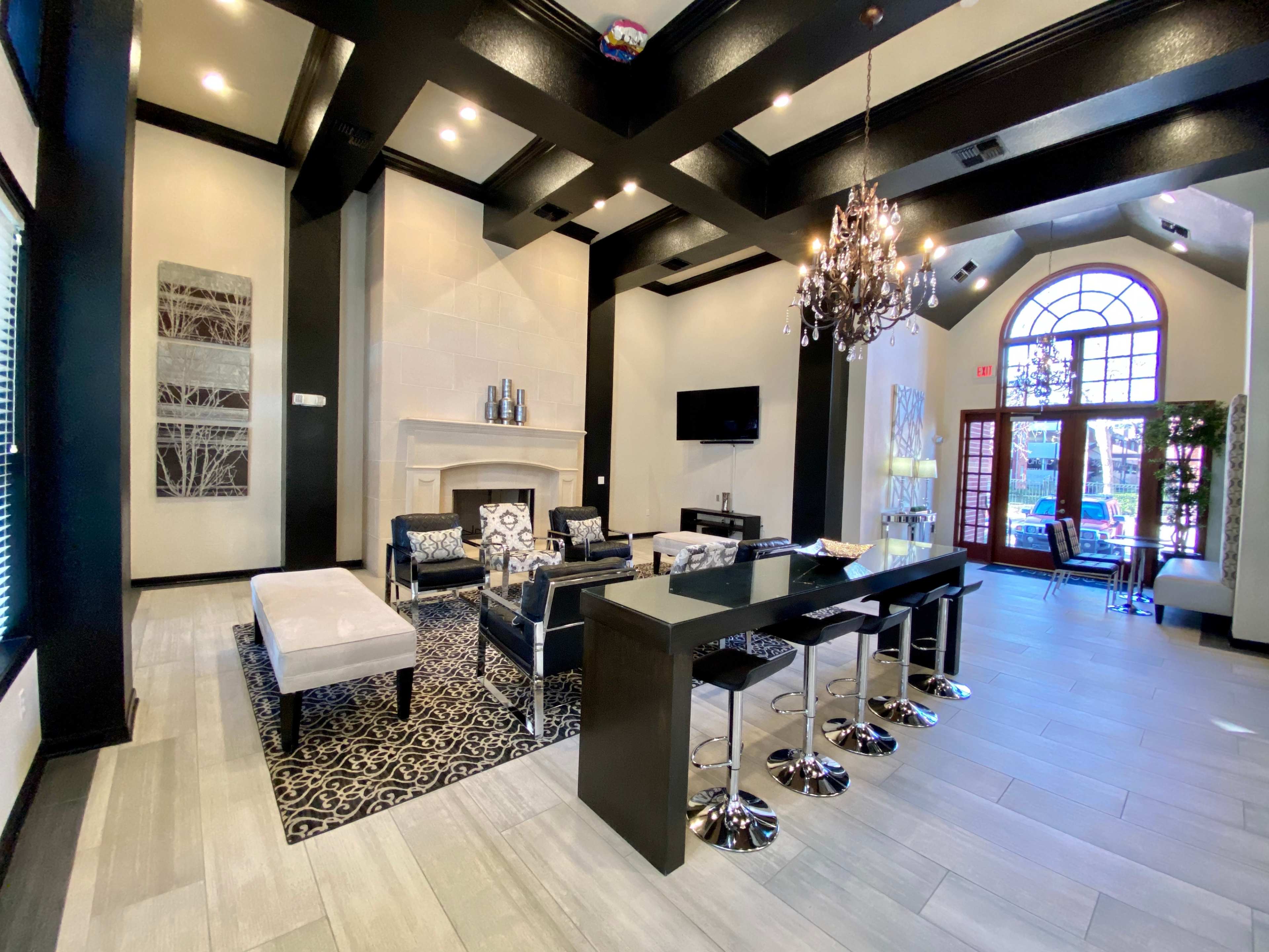 The image shows a modern lounge area featuring seating arrangements, a fireplace, a large window, and a dining table with high stools.