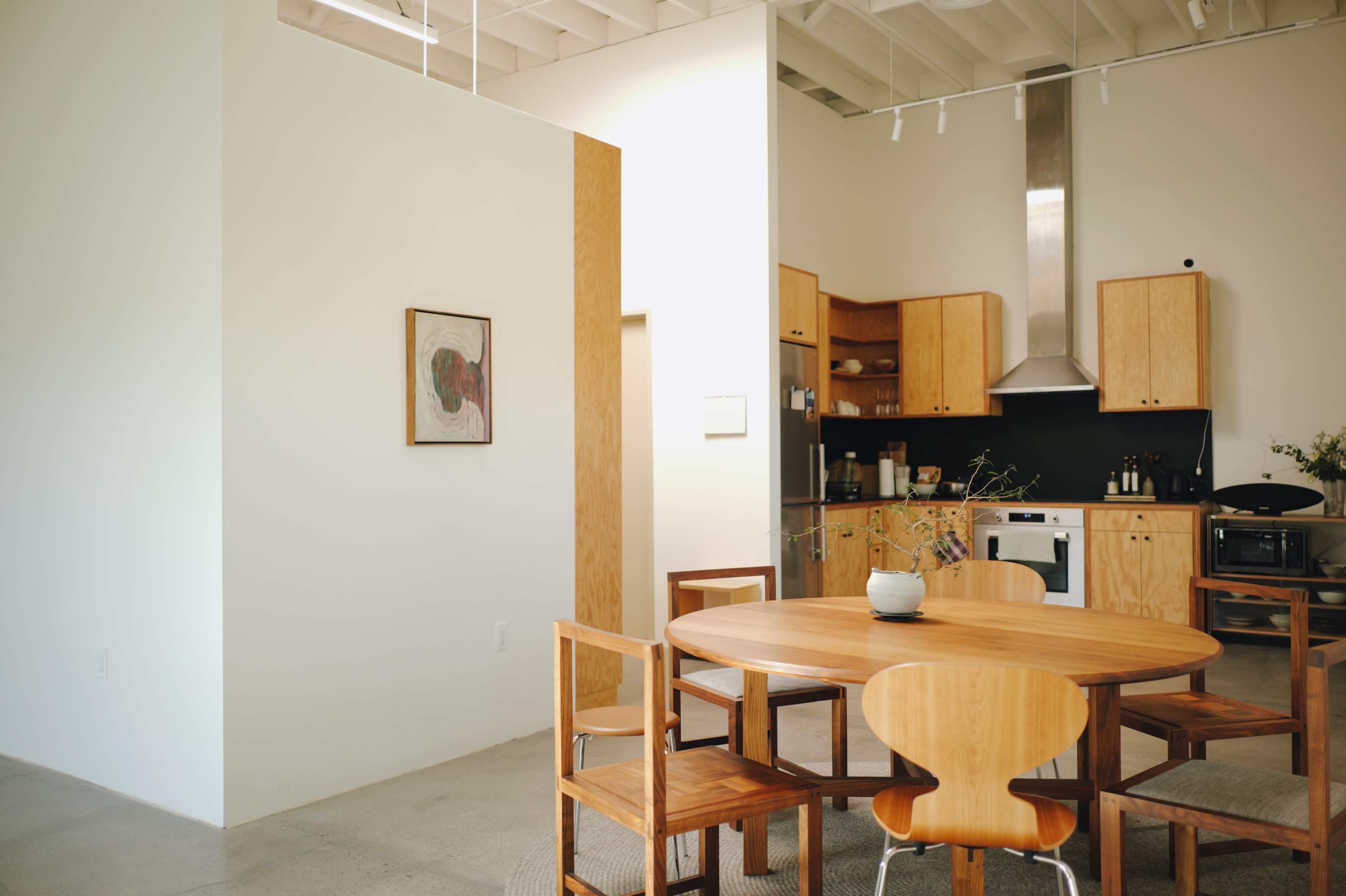 A modern kitchen and dining area features wooden furniture, a round table, and a minimalist design.