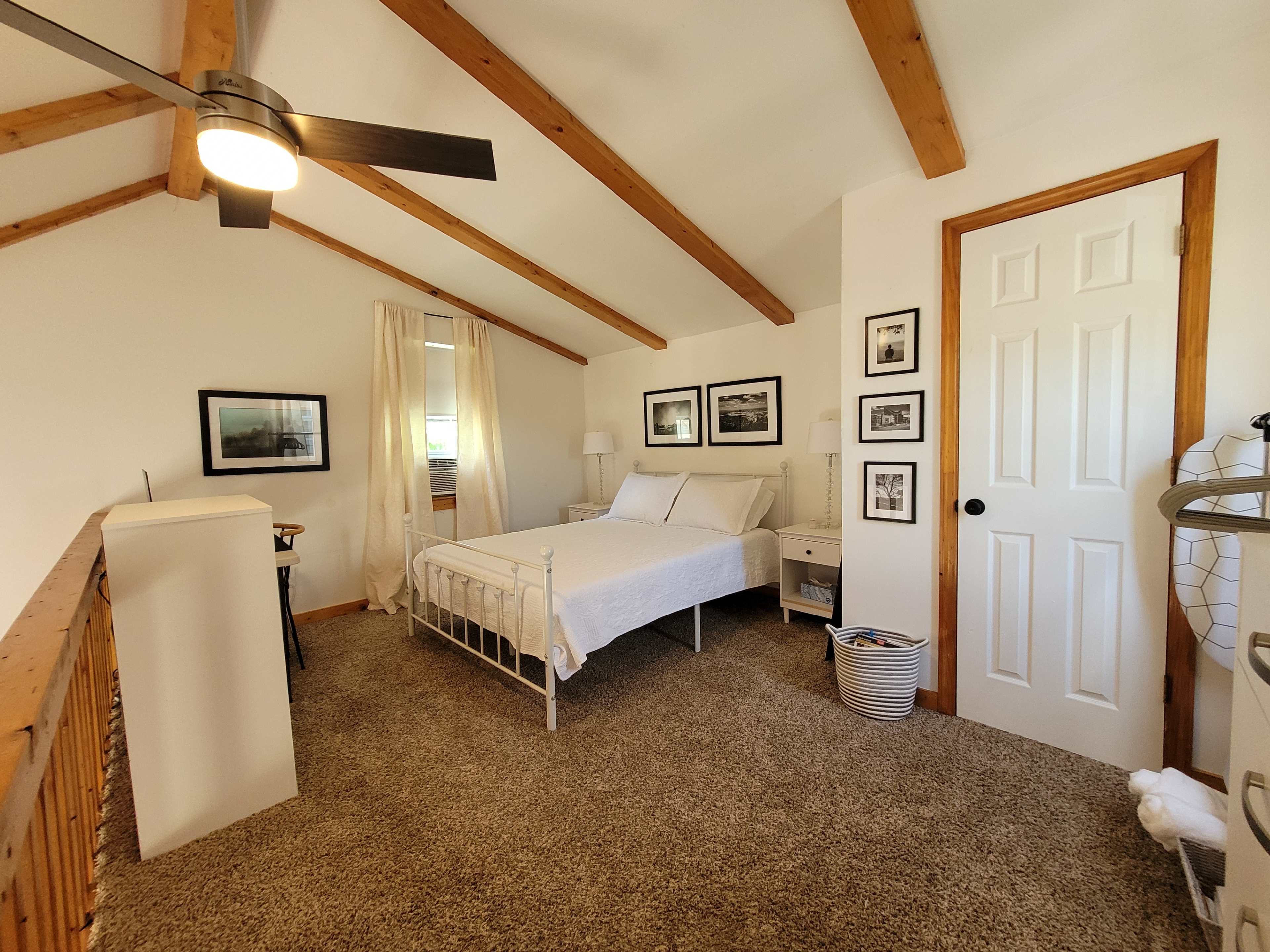 A bedroom with a vaulted ceiling, featuring a white metal bed, wooden beams, and framed pictures on the walls.