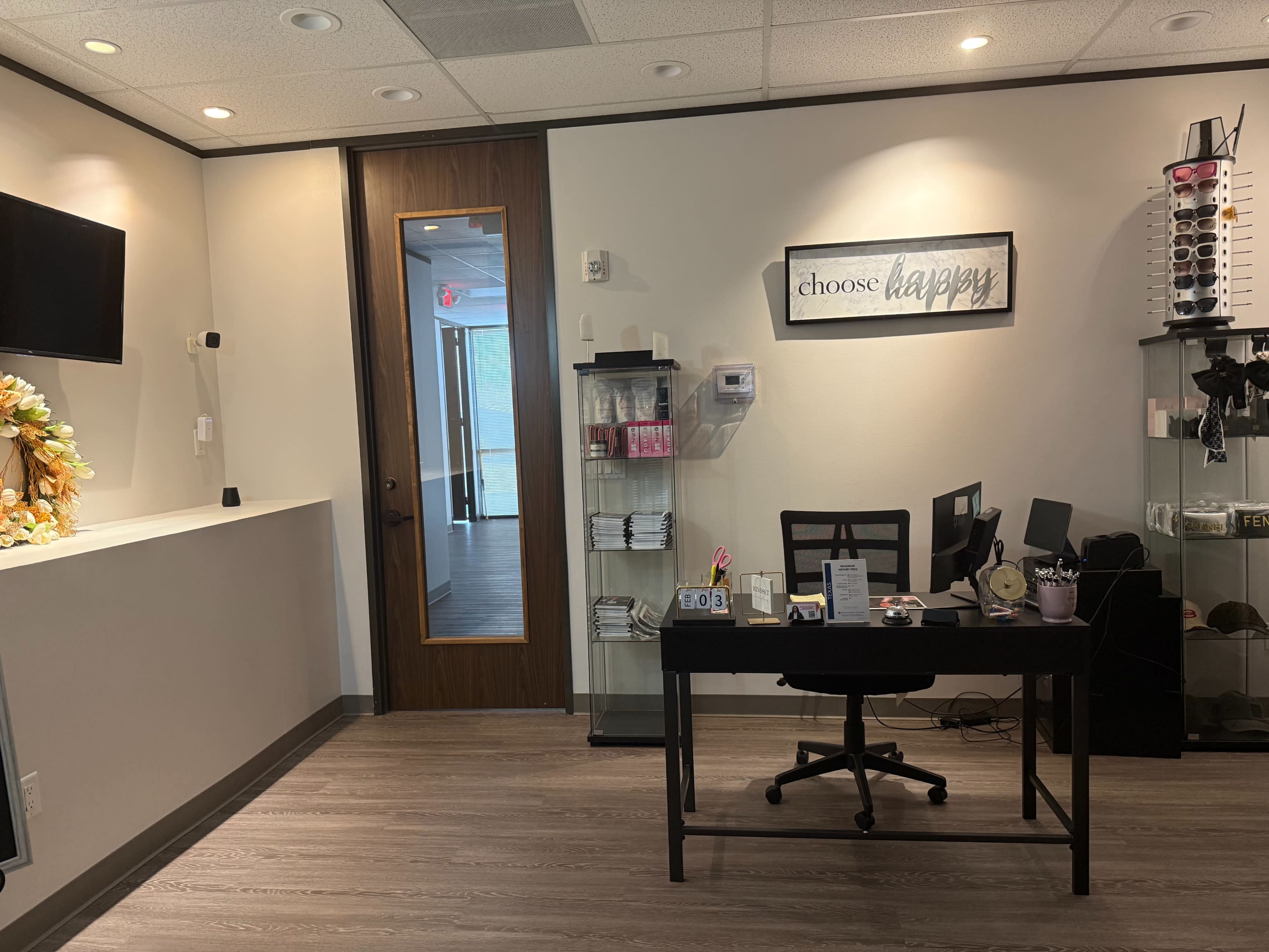 The image shows a small office space with a black desk, a chair, and decorative items on the walls, including a sign that reads "choose happy."