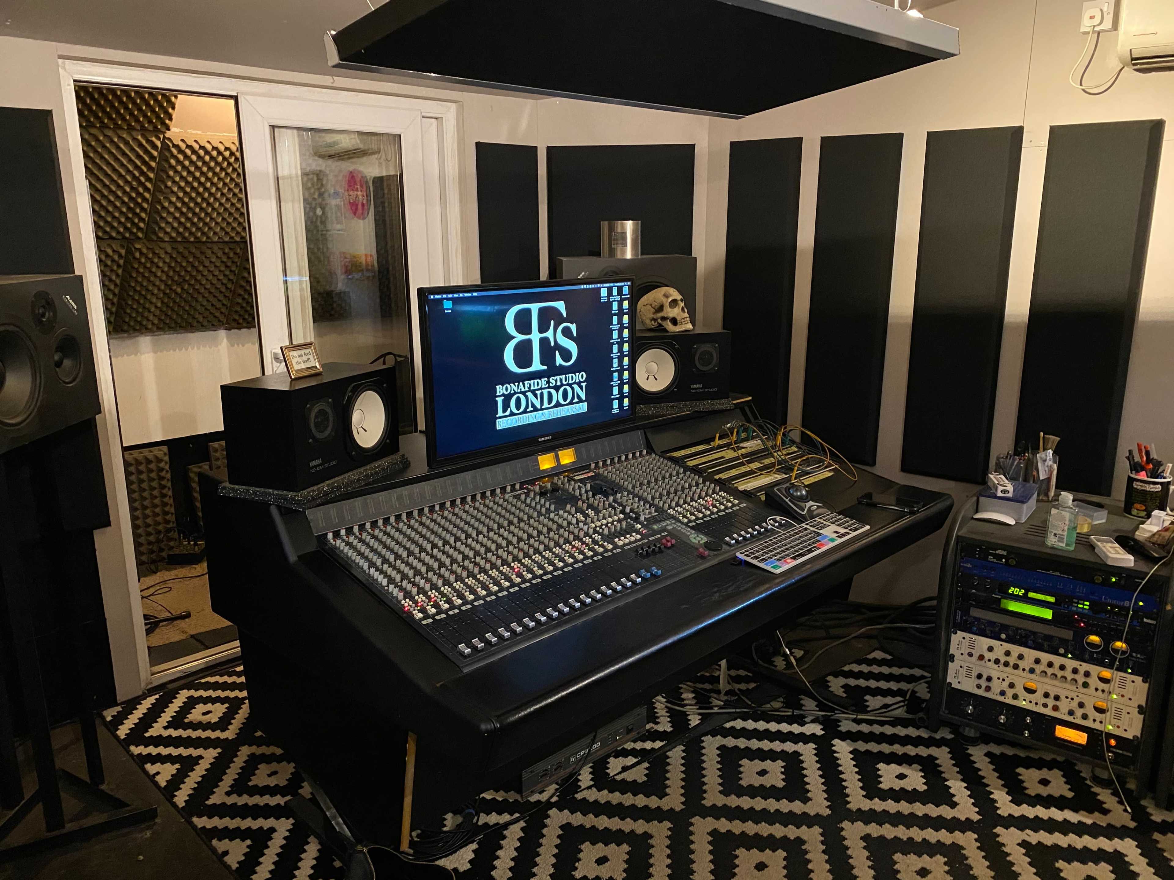 A recording studio with a large mixing console, studio monitors, and soundproofing panels on the walls.