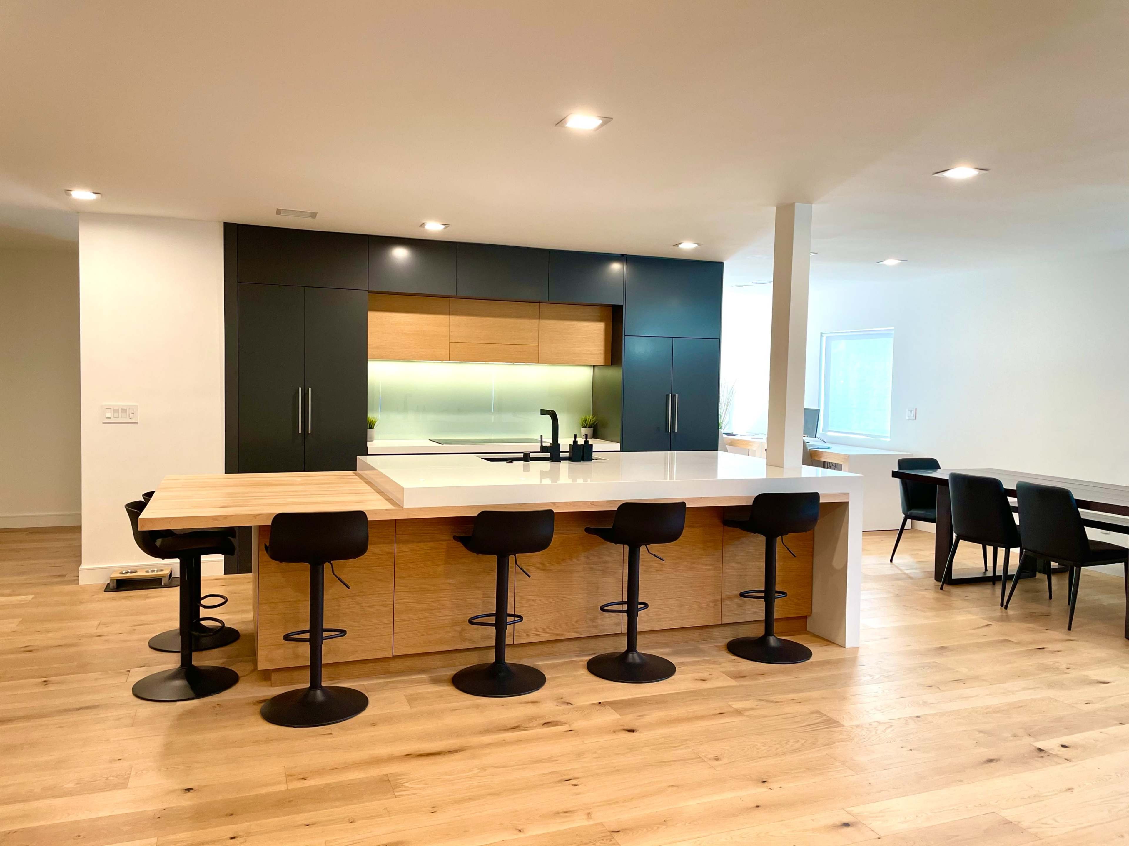 A modern kitchen with a large island featuring black stools and a combination of dark cabinetry and light wood accents.