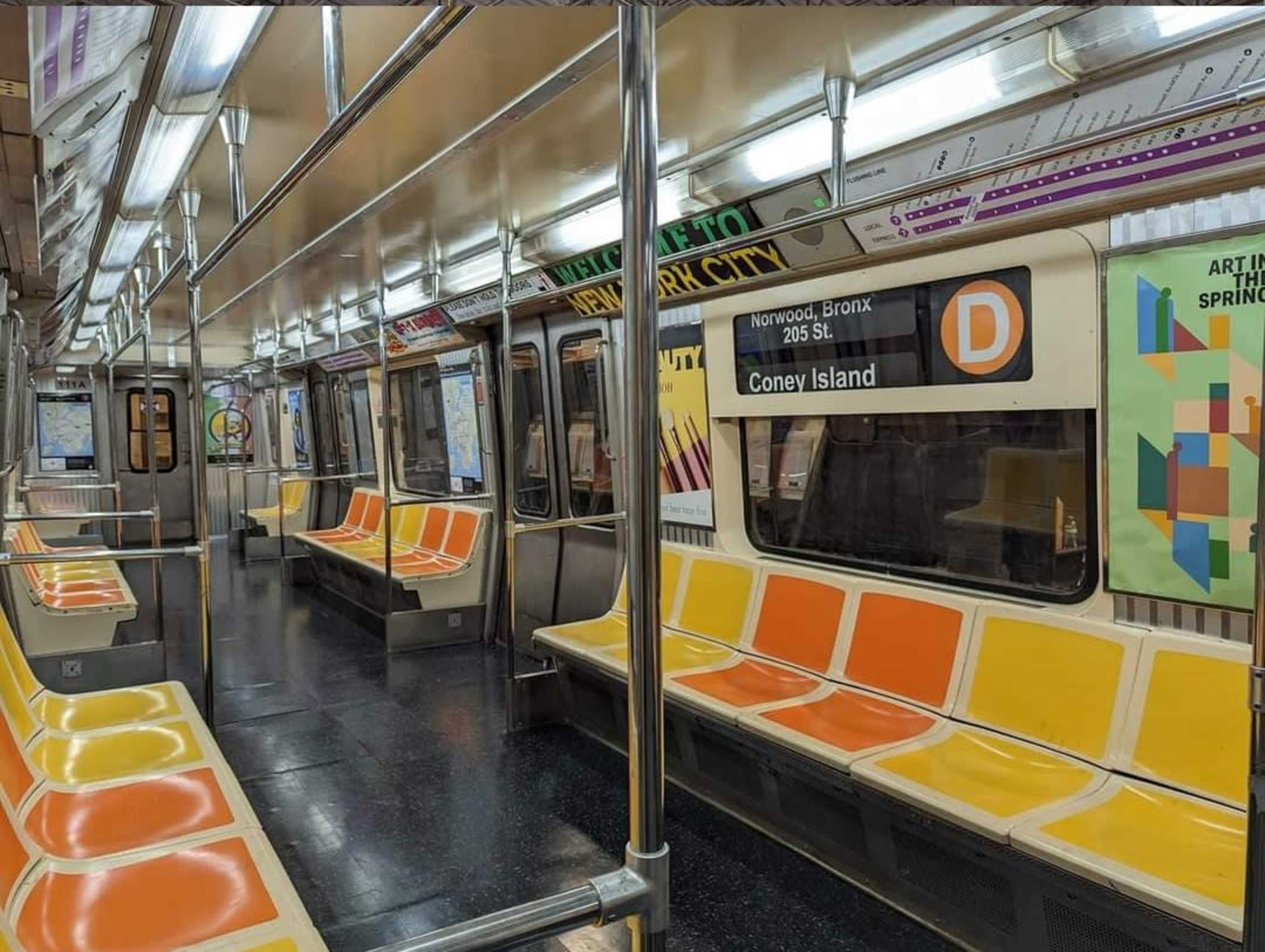 An empty subway car with orange and yellow seating and signage indicating the route to Coney Island.