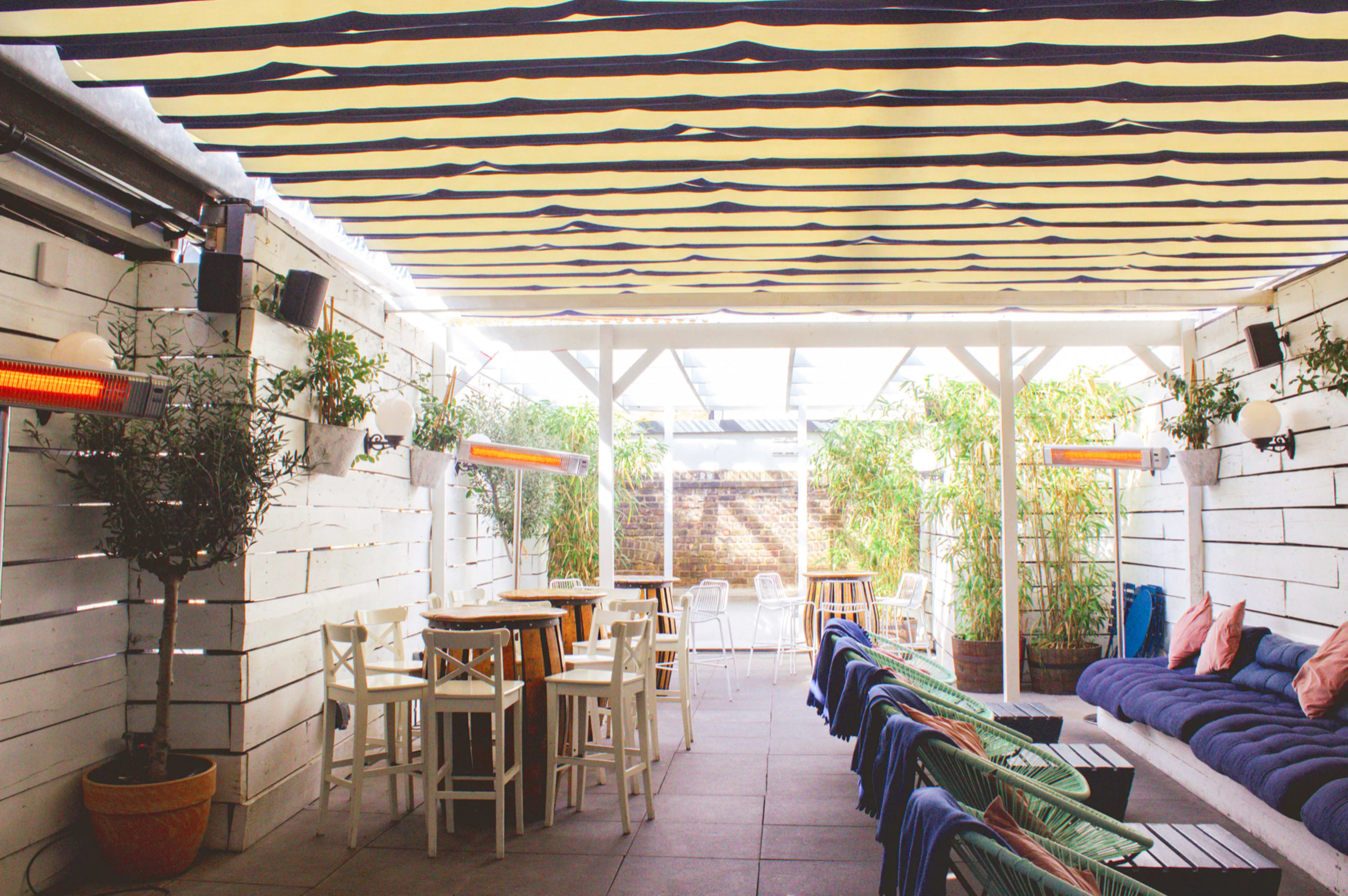 A modern outdoor seating area with striped canopies, wooden furniture, and potted plants.
