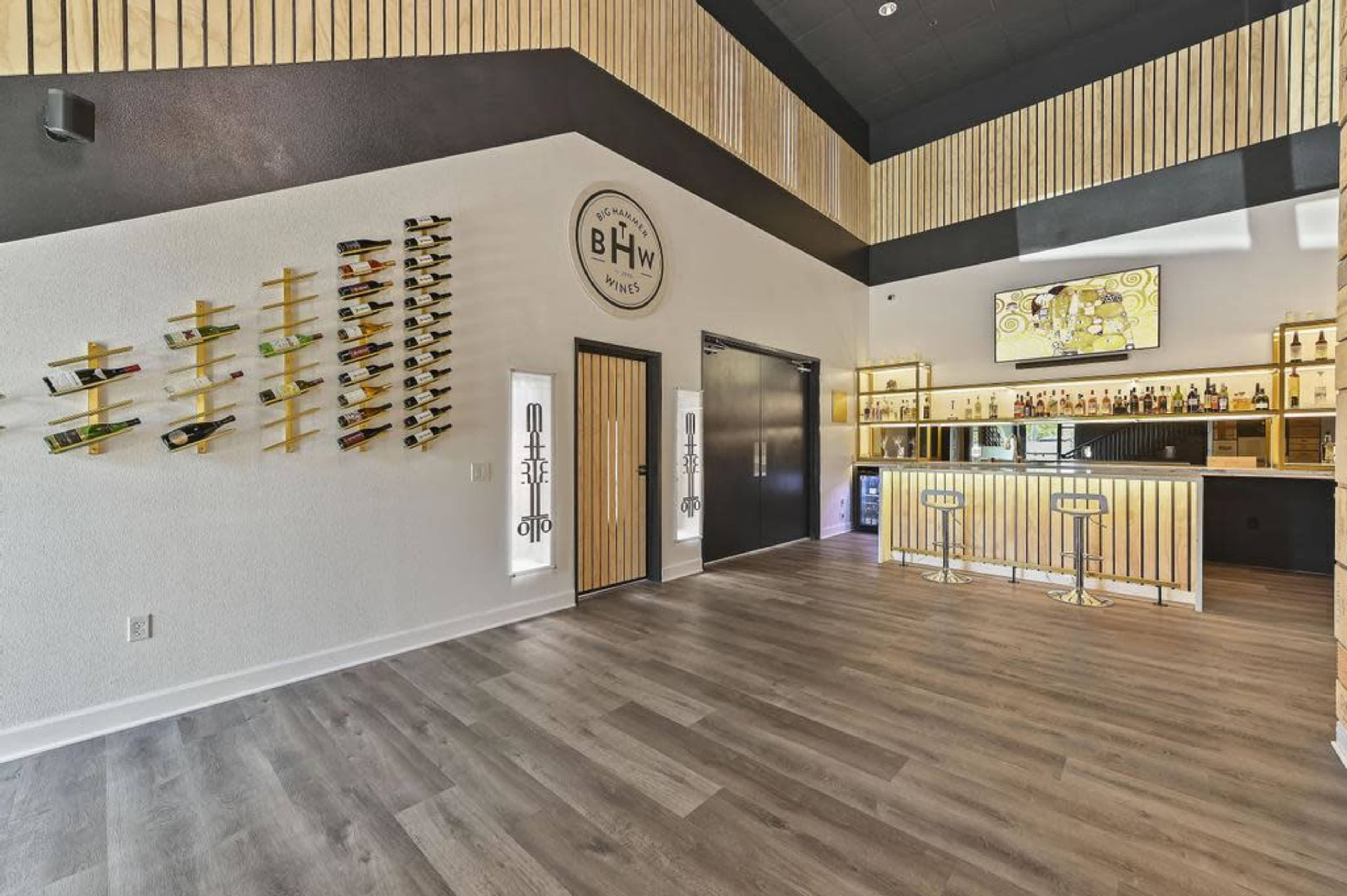 A modern bar interior featuring a wooden drink display on the wall, a well-lit bar counter, and a large television screen.