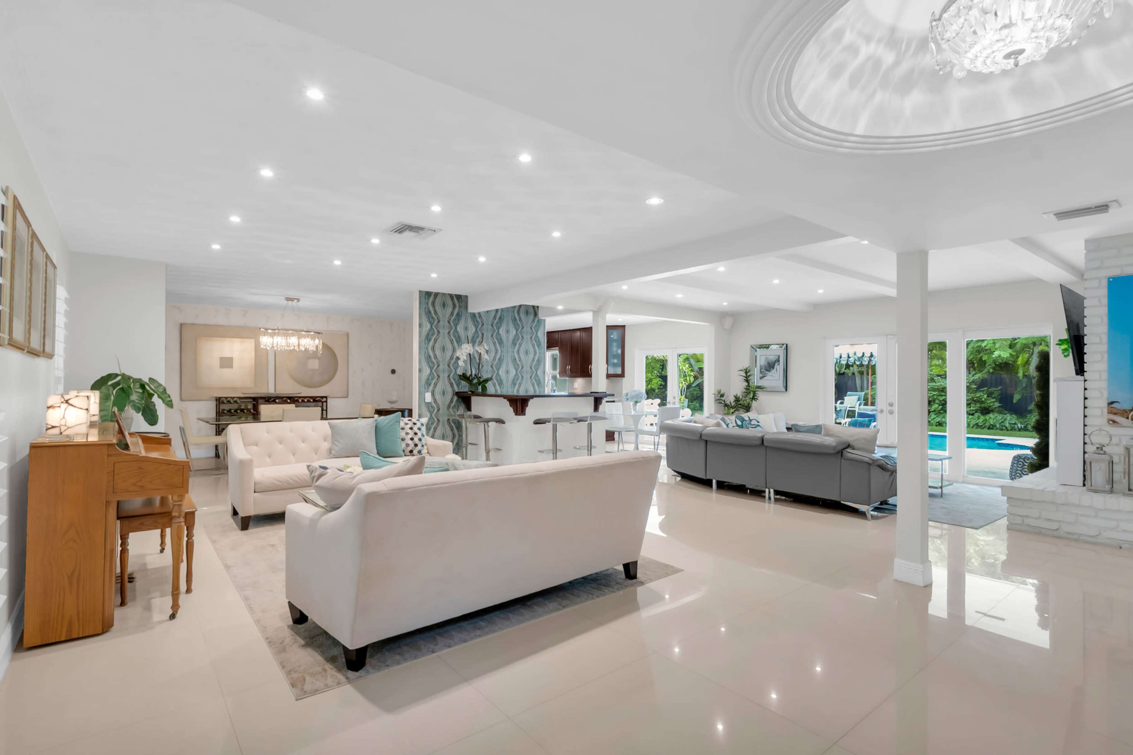 The image shows a modern open-concept living space with a cozy seating area, a dining area, and a view of a pool through large windows.